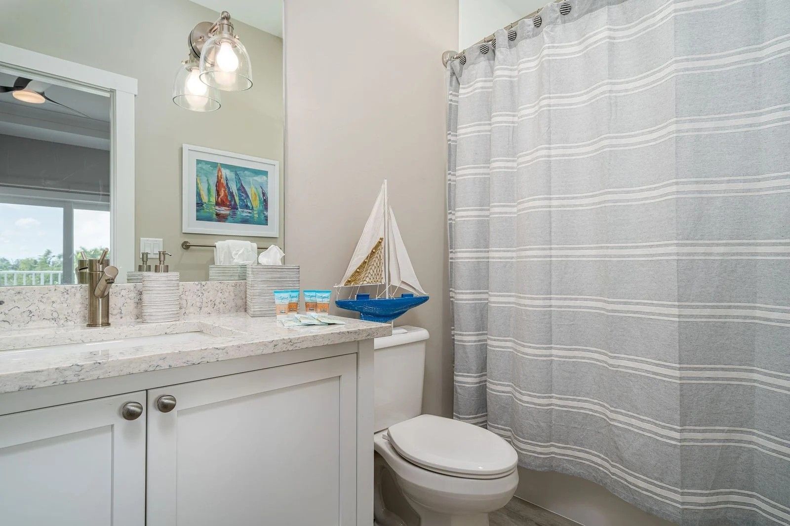 Bathroom with white vanity, mirror, sink, and a gray shower curtain beside a toilet.