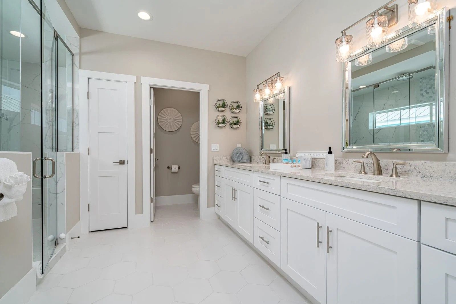 Bright white bathroom with double vanity, large mirrors, glass shower, and beige tiled floor.