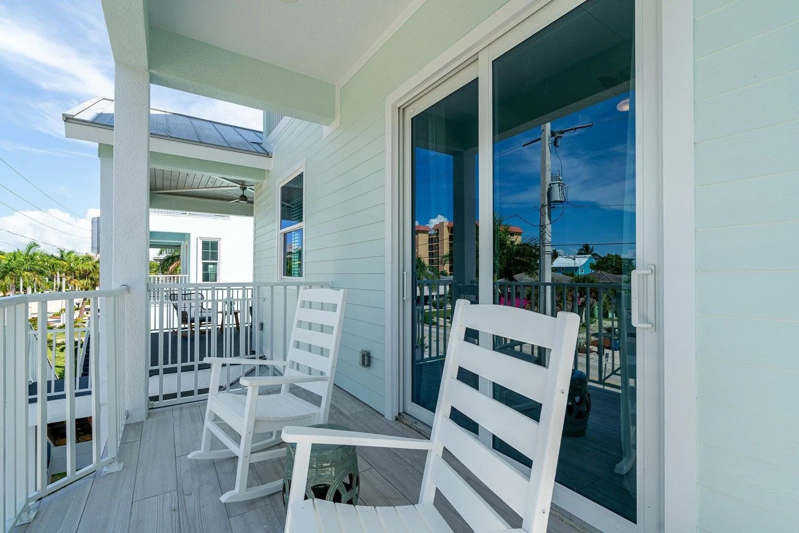 White porch with two chairs and a small table beside sliding glass doors and a blue sky view.