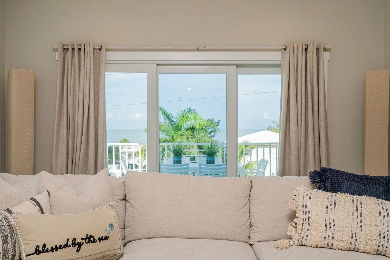 Bright living room with a cream sofa facing a window and beige curtains, ocean view outside.