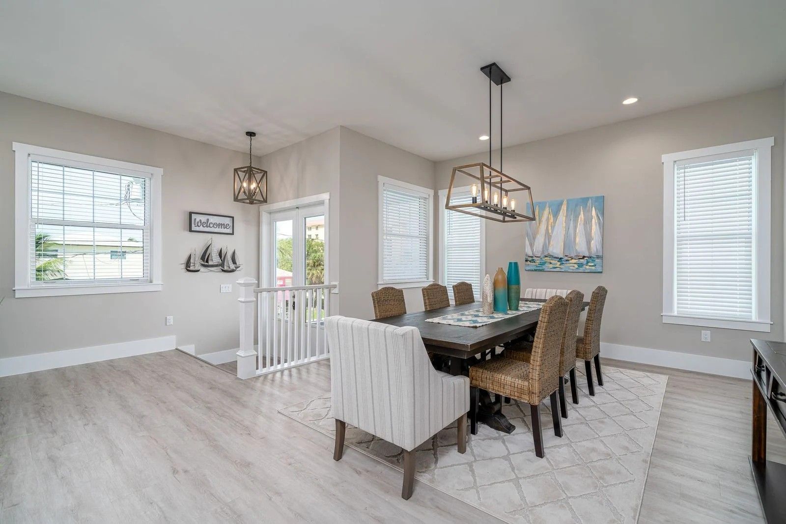 Bright dining room with a dark table, upholstered chairs, white shutters, and pendant lighting