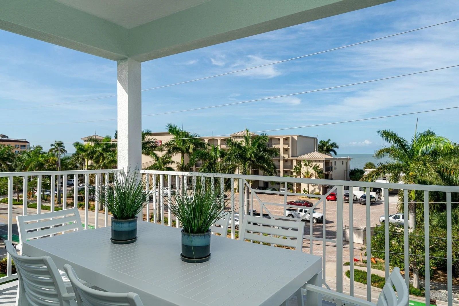 Balcony with white table and chairs overlooking palm trees and the ocean under a blue sky