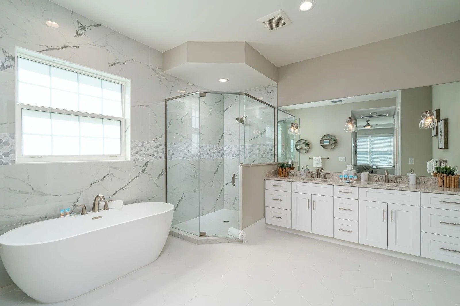 Bright luxury bathroom with freestanding tub, glass shower, double vanity, and marble tile walls