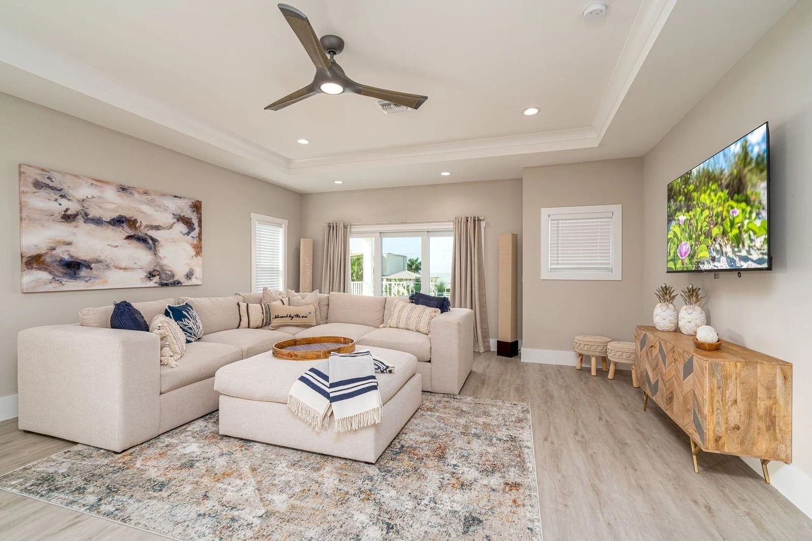 Bright modern living room with sectional sofa, patterned rug, ceiling fan, and wall-mounted TV
