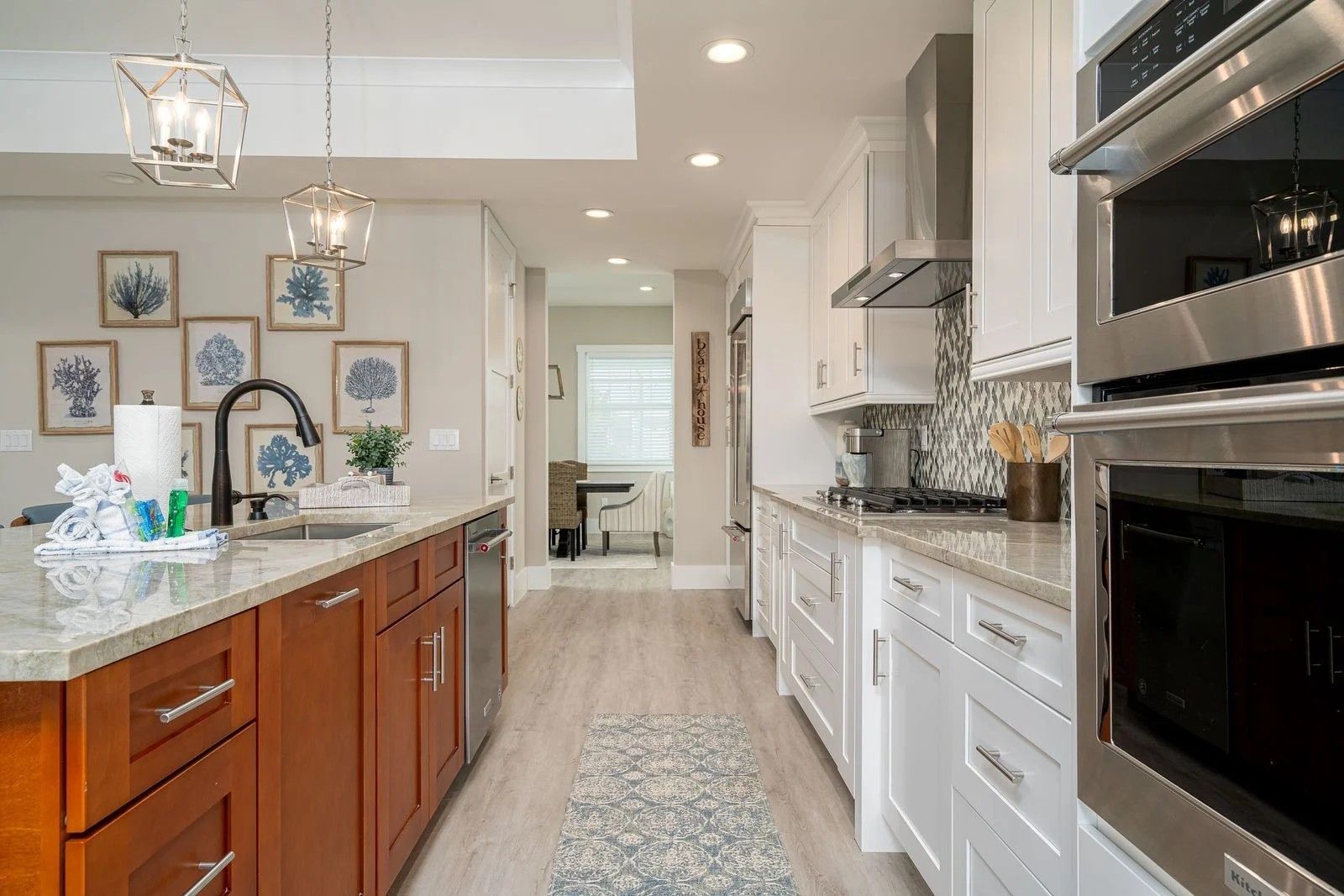 Bright modern kitchen with white and wood cabinets, granite island, pendant lights, and built-in ovens