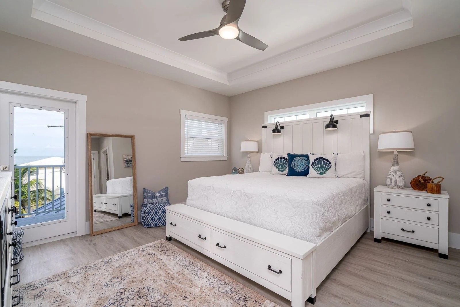 Bright white bedroom with a bed, nightstands, mirror, chair, and balcony doors