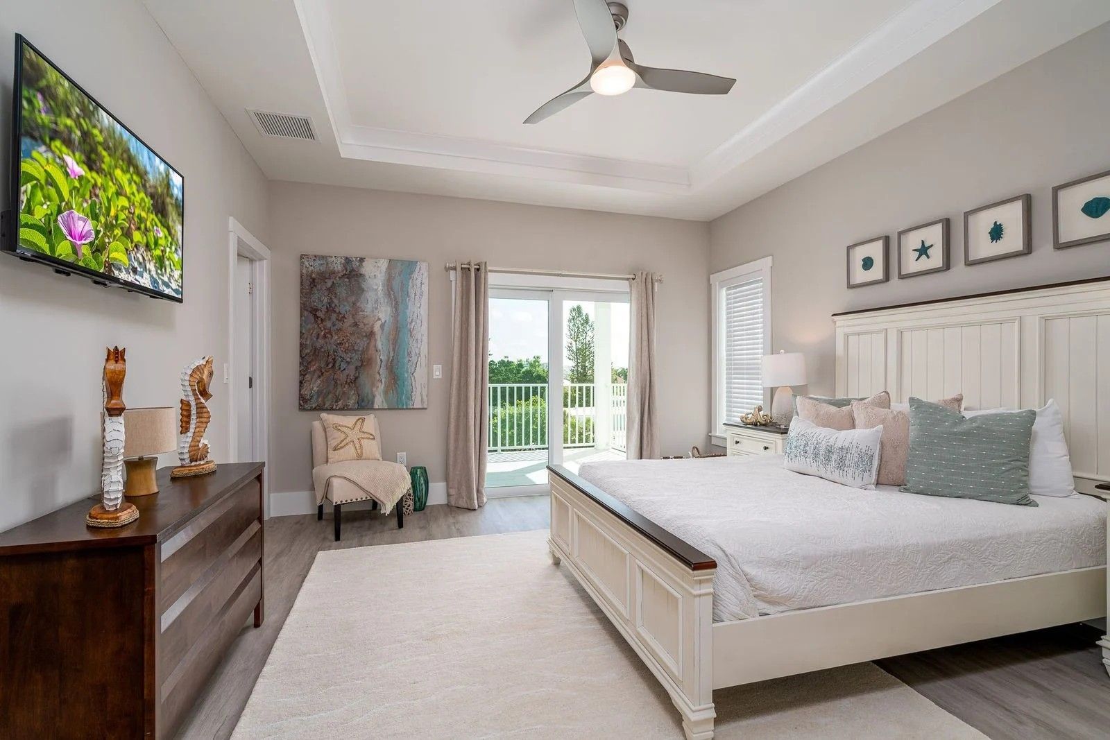 Bright modern bedroom with a king bed, white decor, wall-mounted TV, and balcony doors