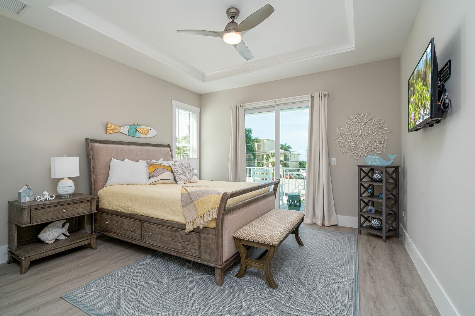 Bright bedroom with a bed, bench, nightstands, ceiling fan, and sliding glass doors to a balcony