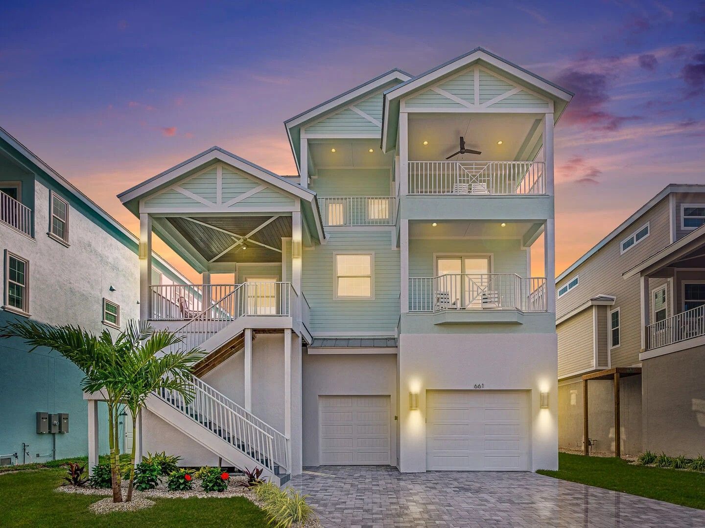 Modern three-story beach house with balconies at sunset, flanked by neighboring homes