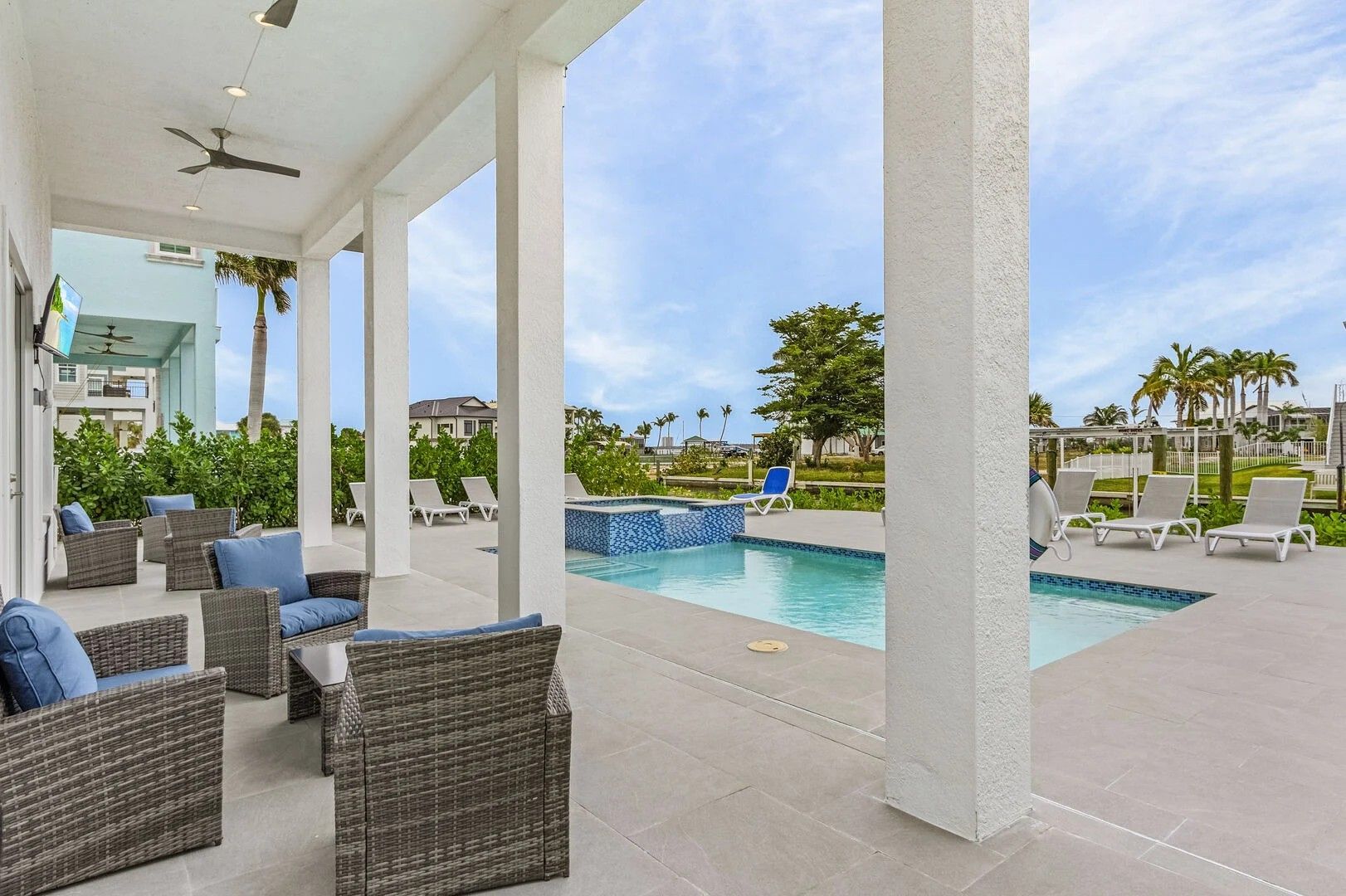 Covered patio with wicker chairs overlooking a backyard pool and lounge chairs under a bright sky