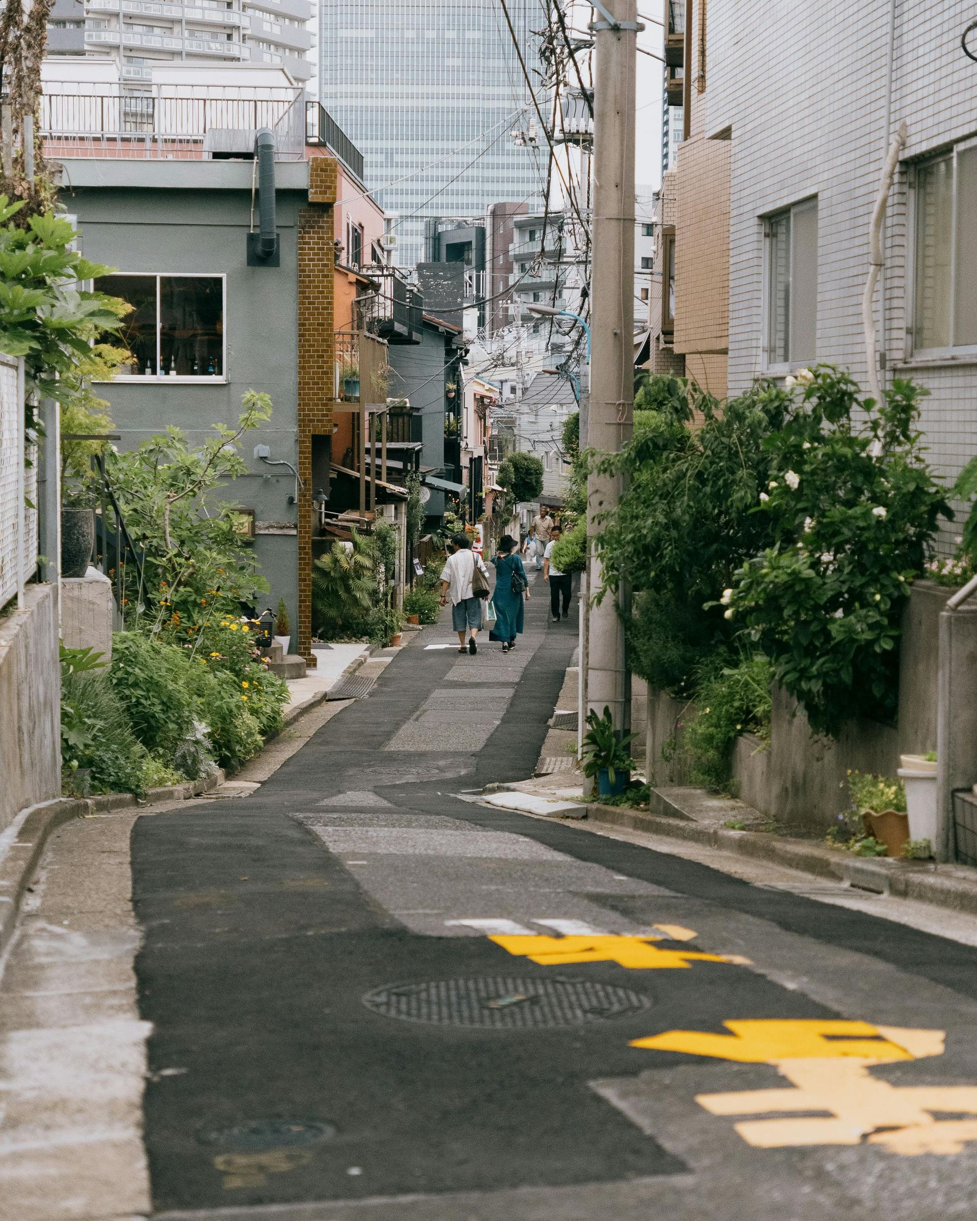 Narrow street in a city, flanked by buildings of varying colors. Two people walk away.