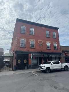 Red brick building with shops on the ground floor, a white pickup truck parked out front, under a cloudy sky.