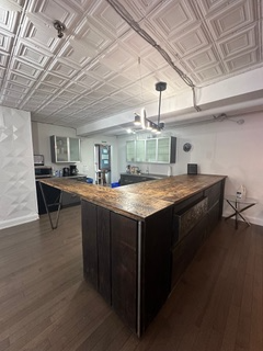 A modern kitchen with a large dark wood island and brown countertop, contrasted by a white tiled ceiling and dark wood flooring.