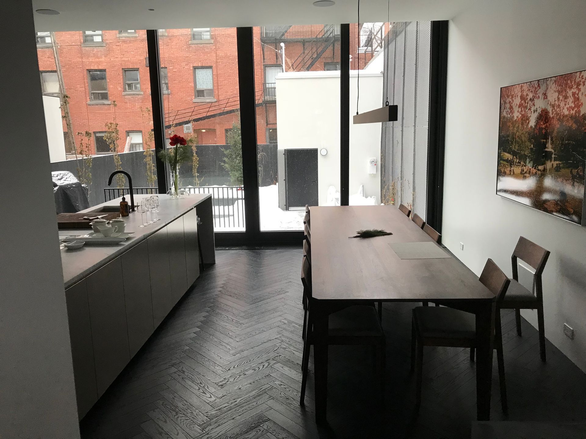 Cuisine et salle à manger modernes avec une longue table, un évier sur îlot et de grandes portes vitrées donnant sur la ville.