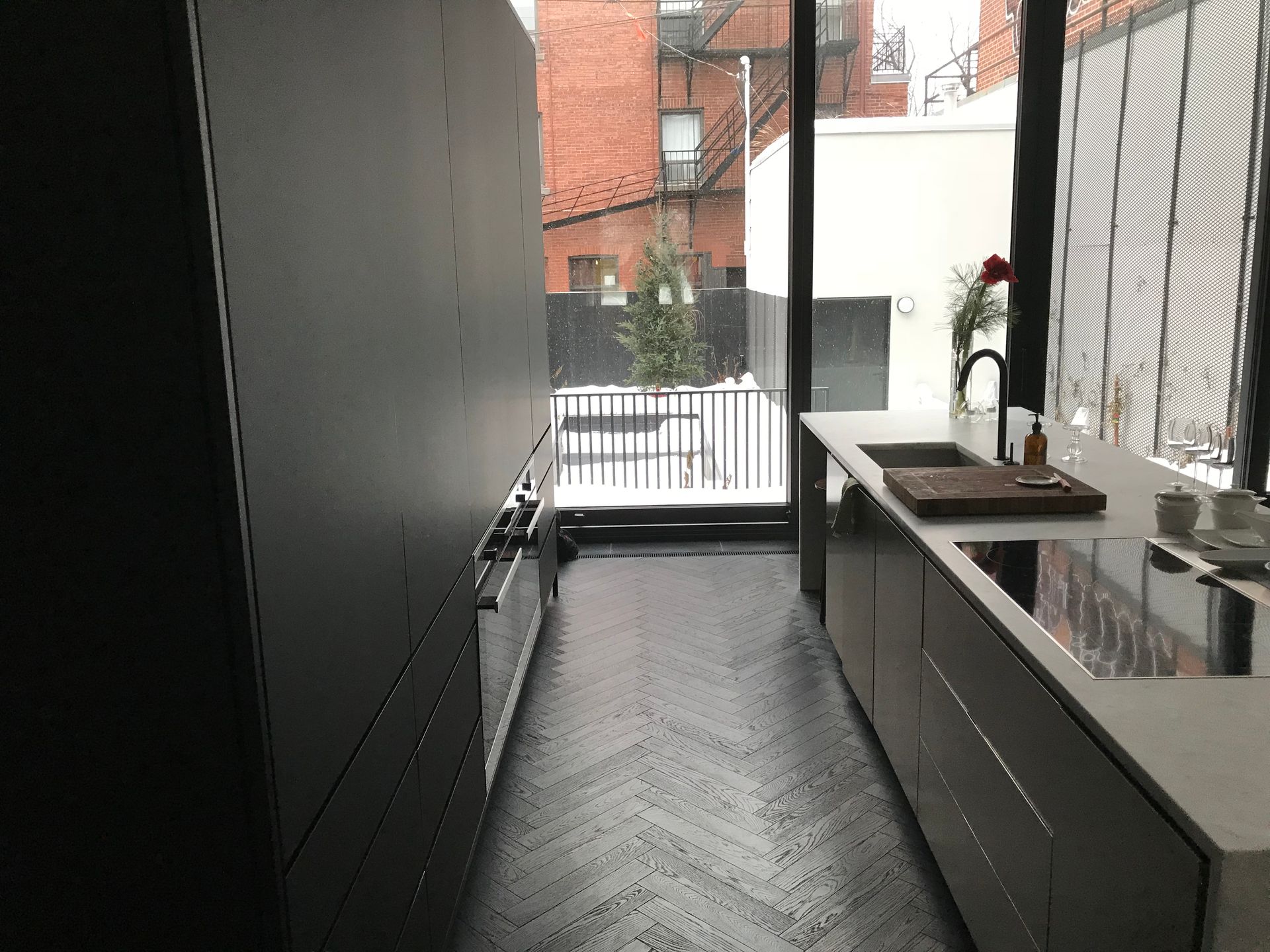 Cuisine moderne étroite avec placards foncés, plan de travail blanc, évier et petit balcon donnant sur le fond.