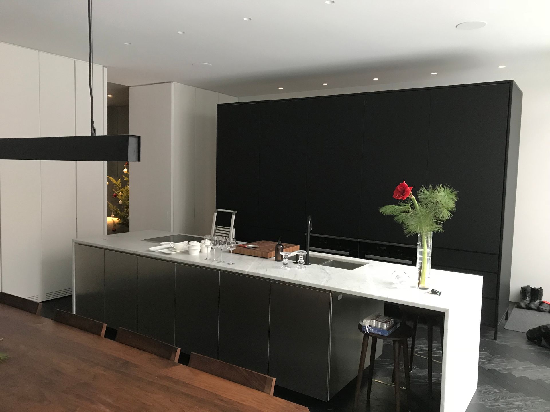 Cuisine moderne avec îlot noir, plans de travail blancs, suspension lumineuse et une fleur rouge dans un vase