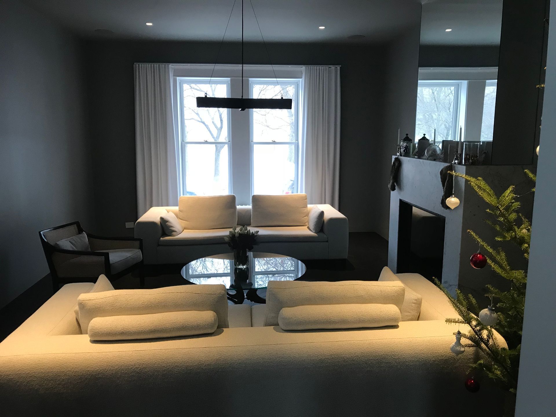Salon moderne avec canapé gris, grande fenêtre, table basse et cheminée décorée de verdure.