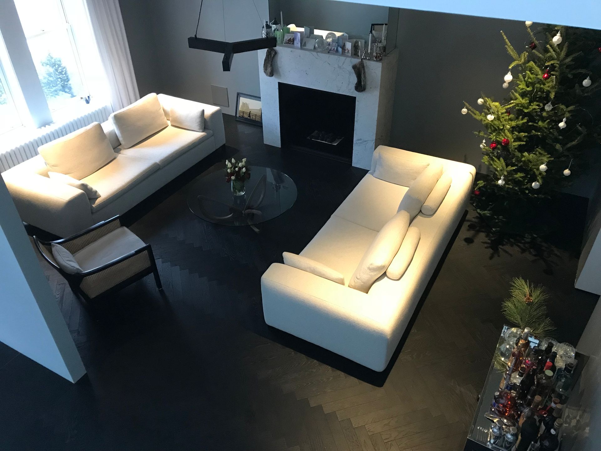 Salon moderne avec canapés blancs, table basse en verre, cheminée et sapin de Noël illuminé