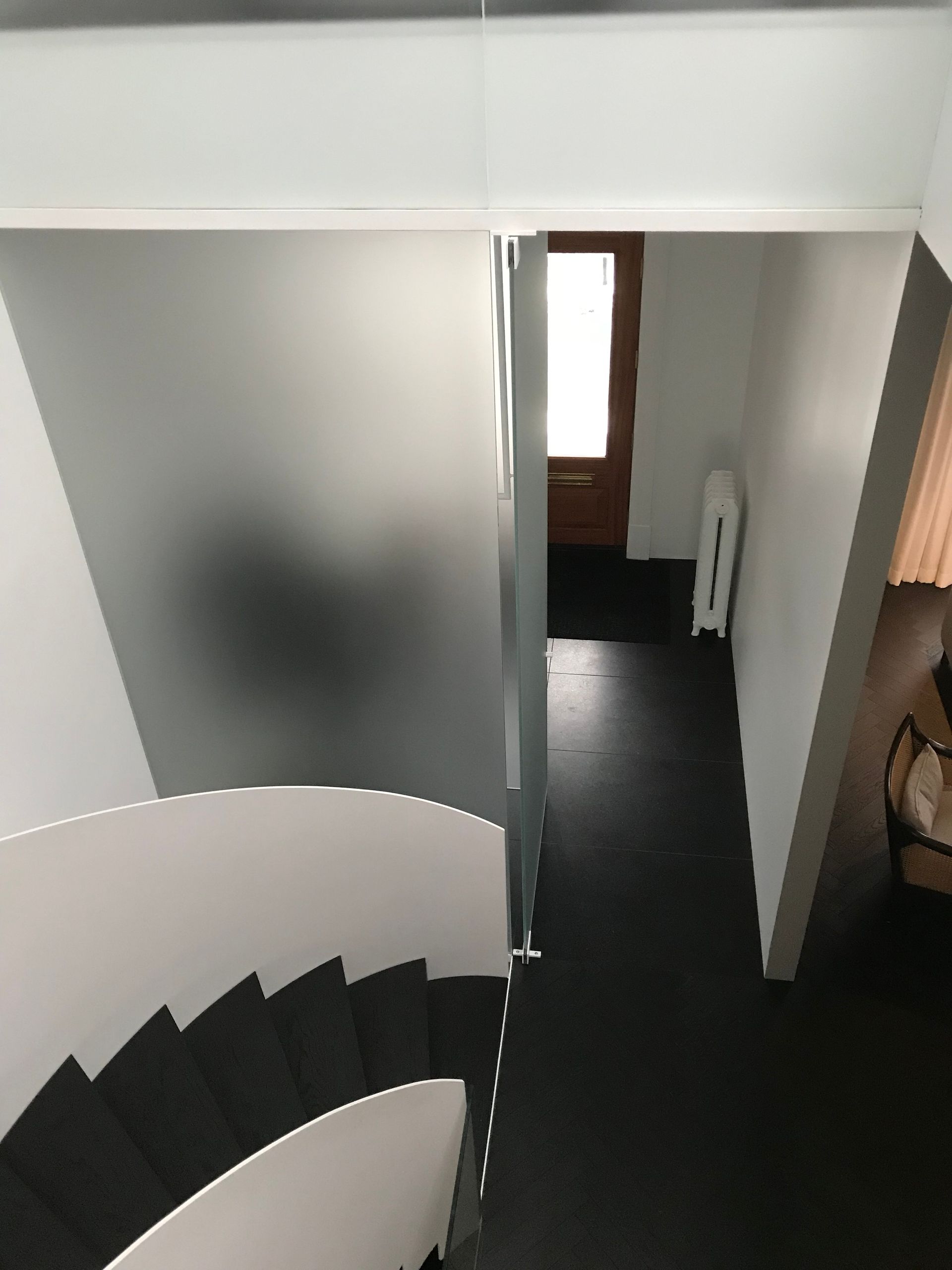 Escalier courbe jouxtant un couloir avec une cloison en verre dépoli et un sol foncé