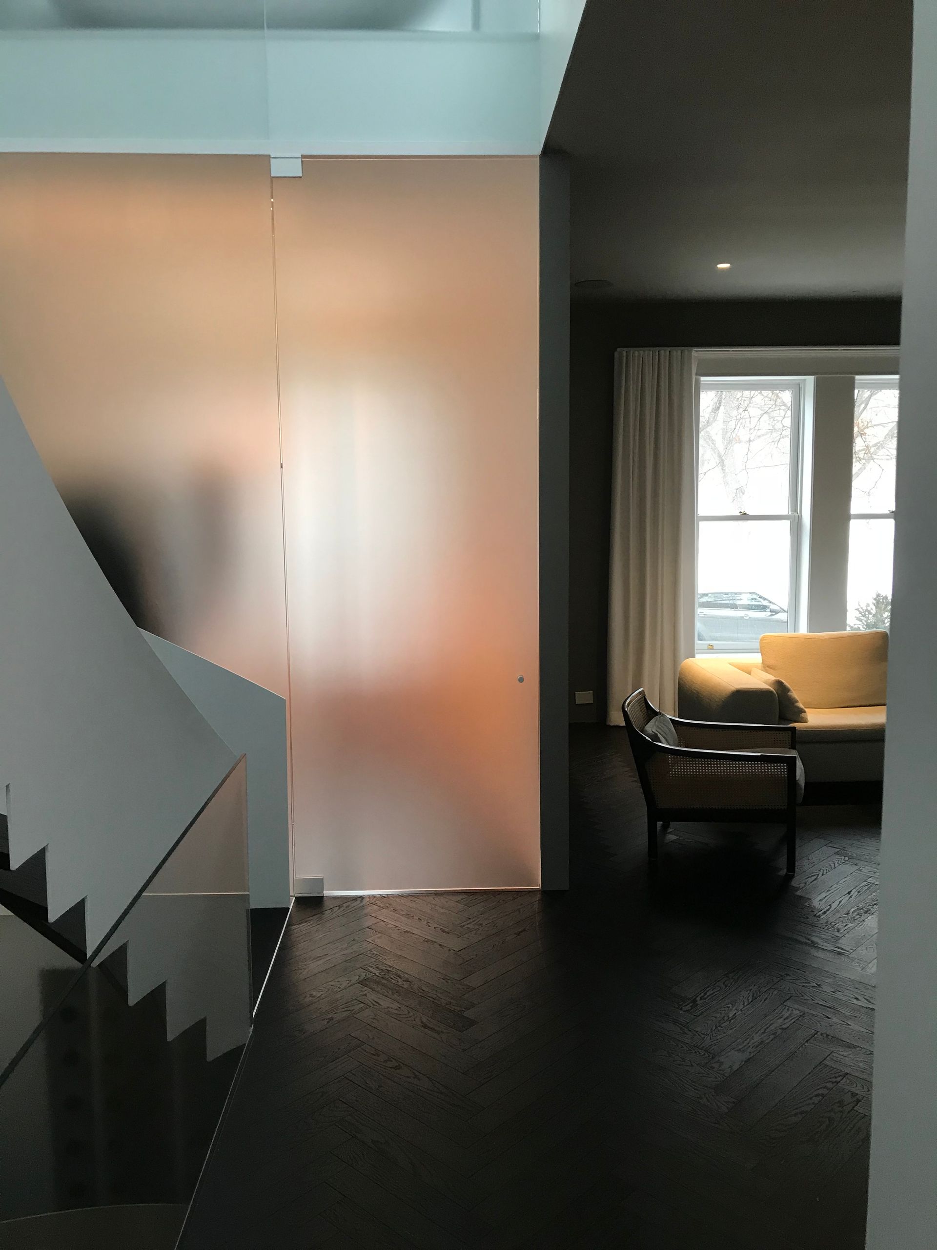 Intérieur moderne avec portes dépolies, un escalier et un coin salon tamisé avec un fauteuil et une fenêtre lumineuse.