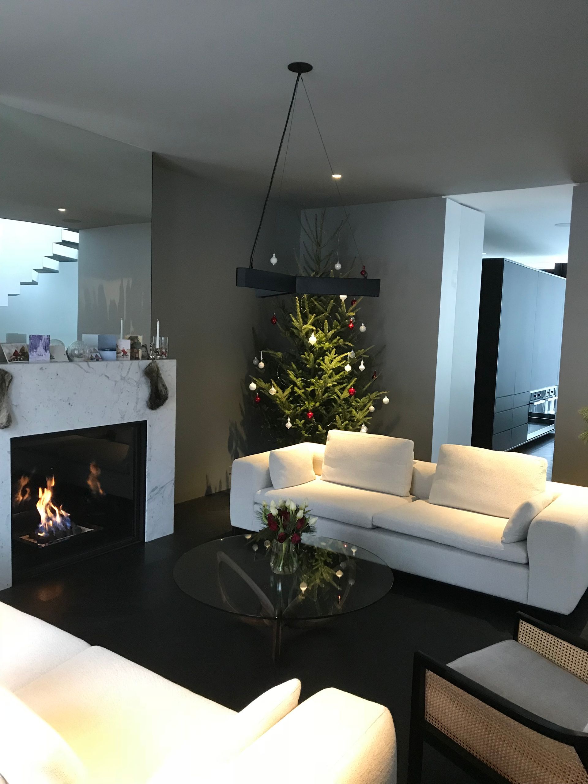 Salon moderne avec cheminée, canapé blanc, table basse en verre et sapin de Noël illuminé