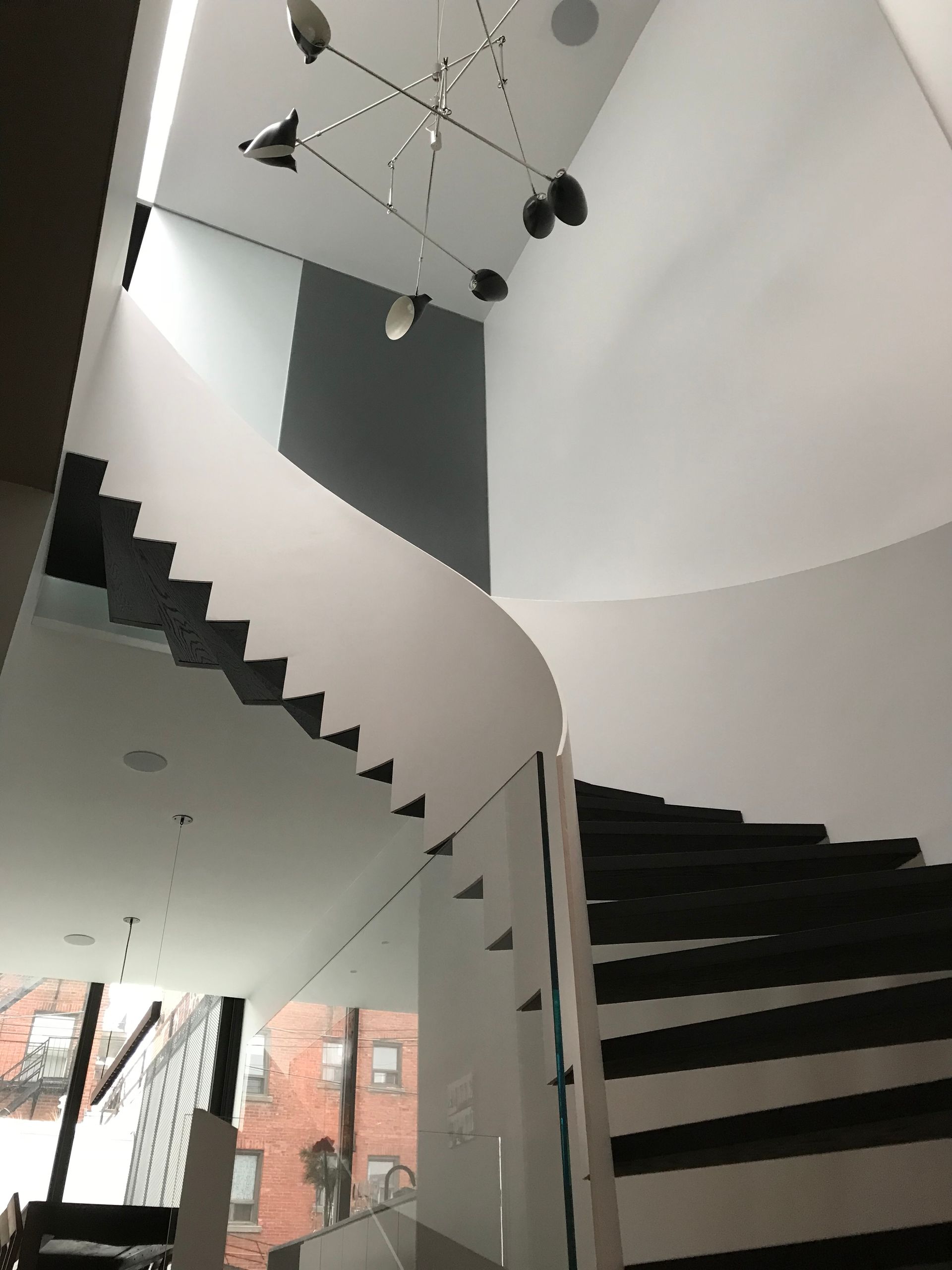 Escalier blanc incurvé aux marches noires dans un atrium moderne, vu d'en bas, avec des luminaires suspendus au plafond