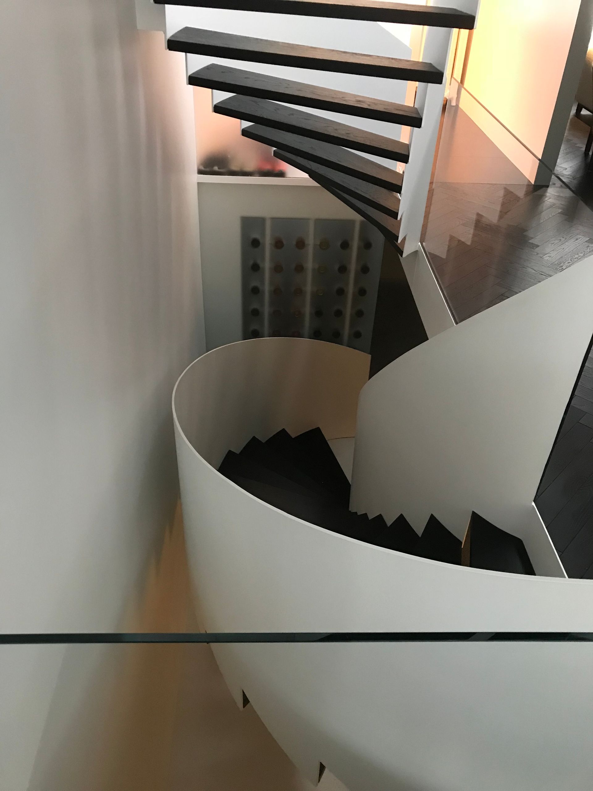 Escalier intérieur incurvé avec marches noires et rampe en spirale blanche, adossé à un mur gris.