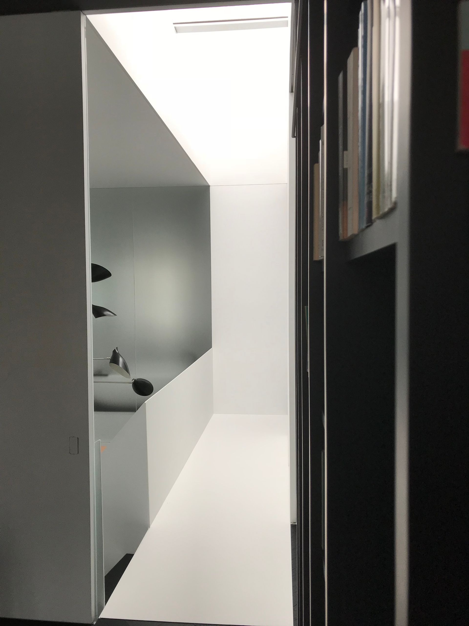 Un couloir étroit aux murs blancs, aux moulures noires et orné de tableaux encadrés, menant à une porte lumineuse.