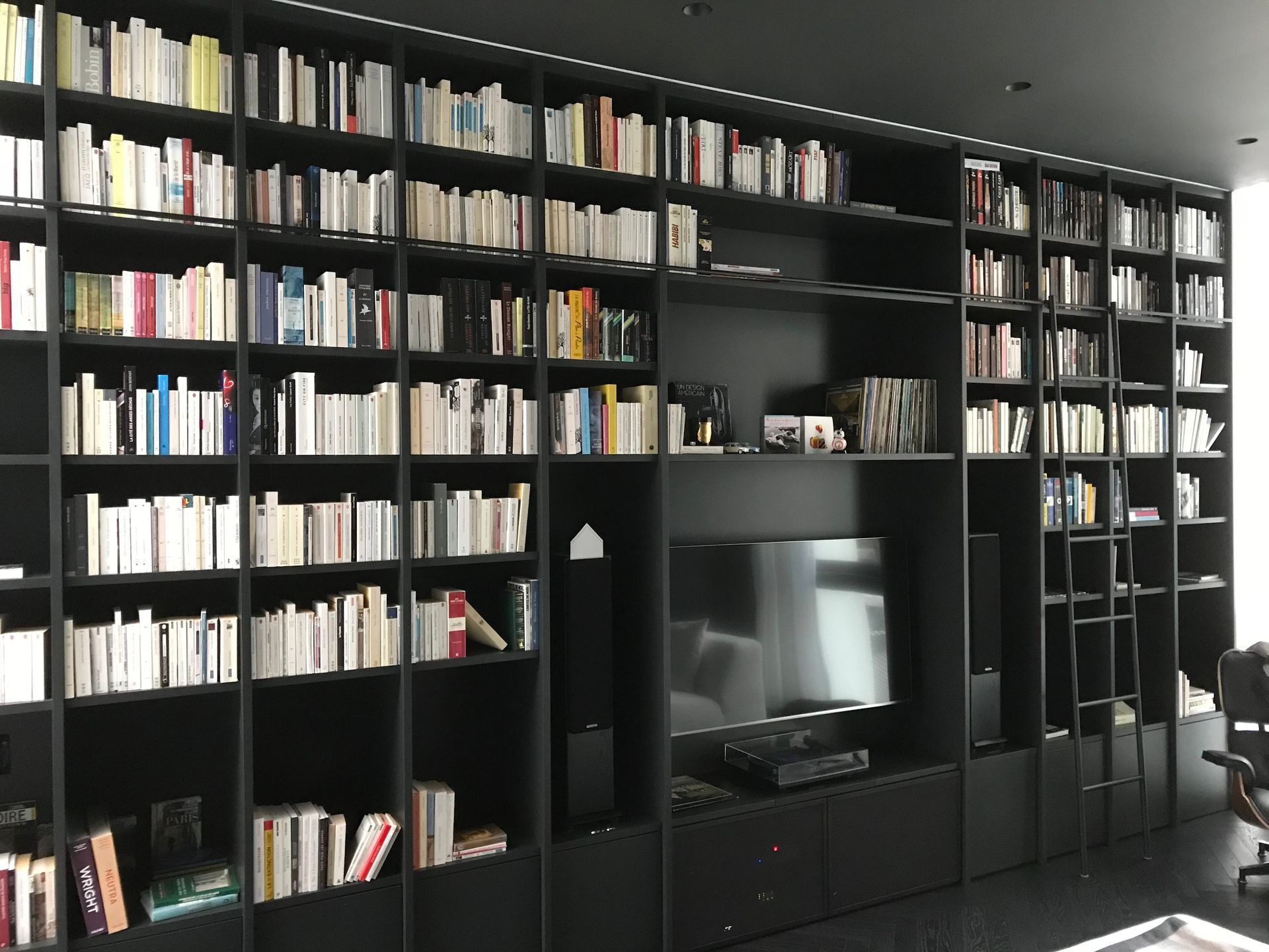 Mur de bibliothèque noire avec livres, télévision et haut-parleurs dans un salon moderne