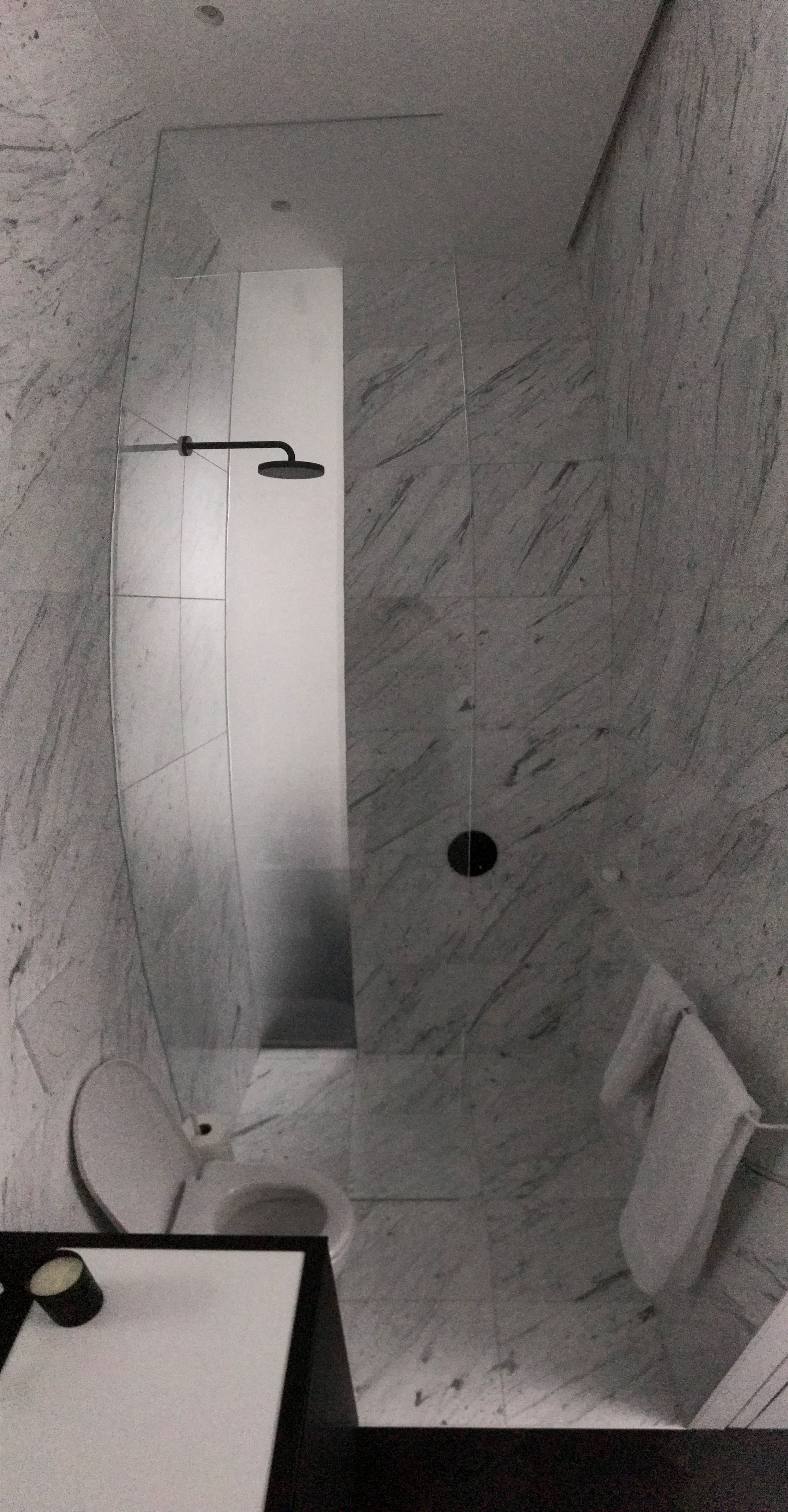 Petite salle de bains moderne avec murs en marbre, douche, toilettes et lavabo visibles.
