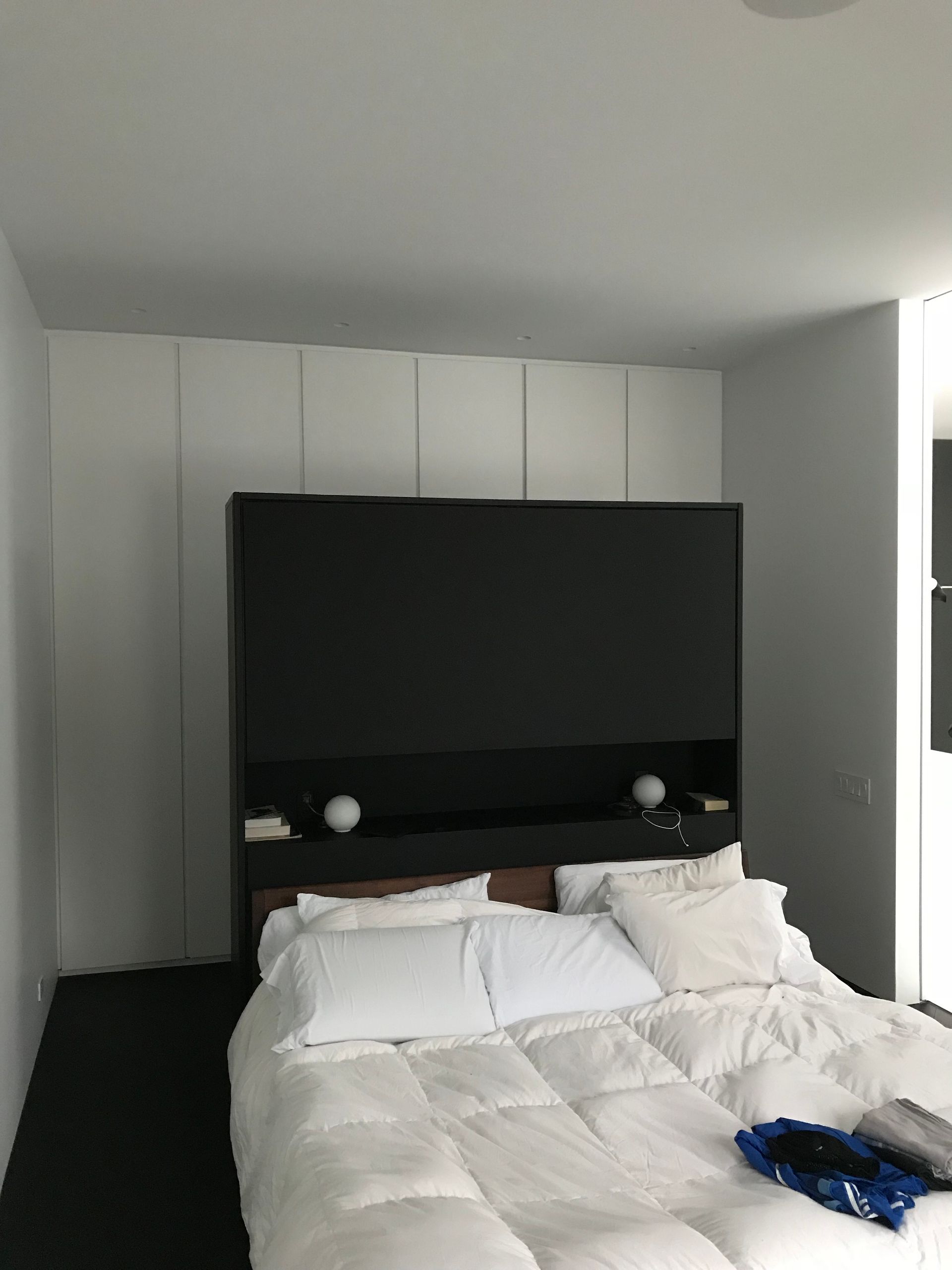 Chambre moderne avec lit blanc défait et grande tête de lit noire sur fond de murs blancs.