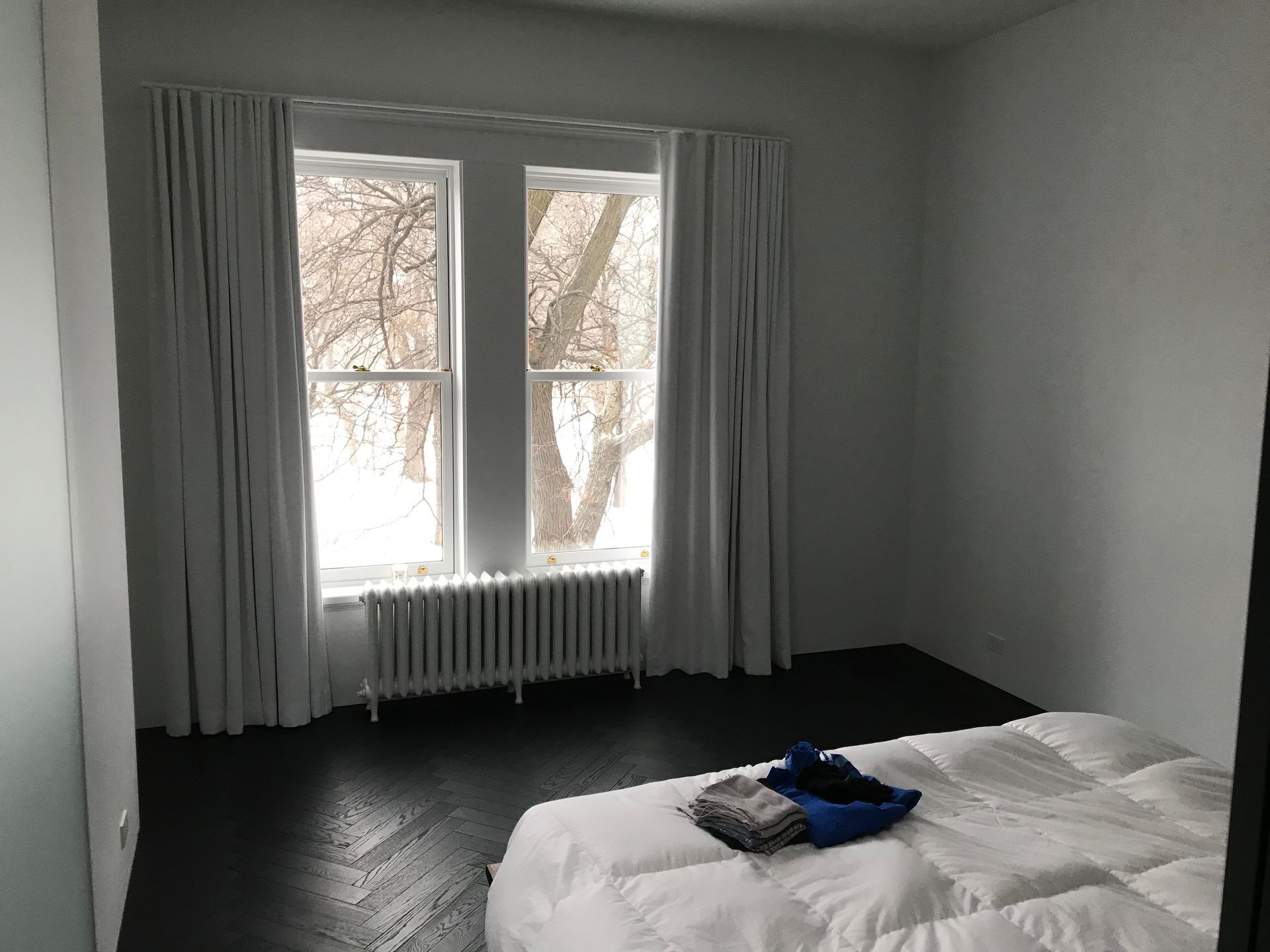 Chambre minimaliste avec lit, sol foncé et grande fenêtre donnant sur des arbres enneigés