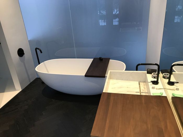 Salle de bains moderne avec baignoire blanche autoportante, sol noir et meuble-lavabo en bois à côté d'une paroi de douche en verre.