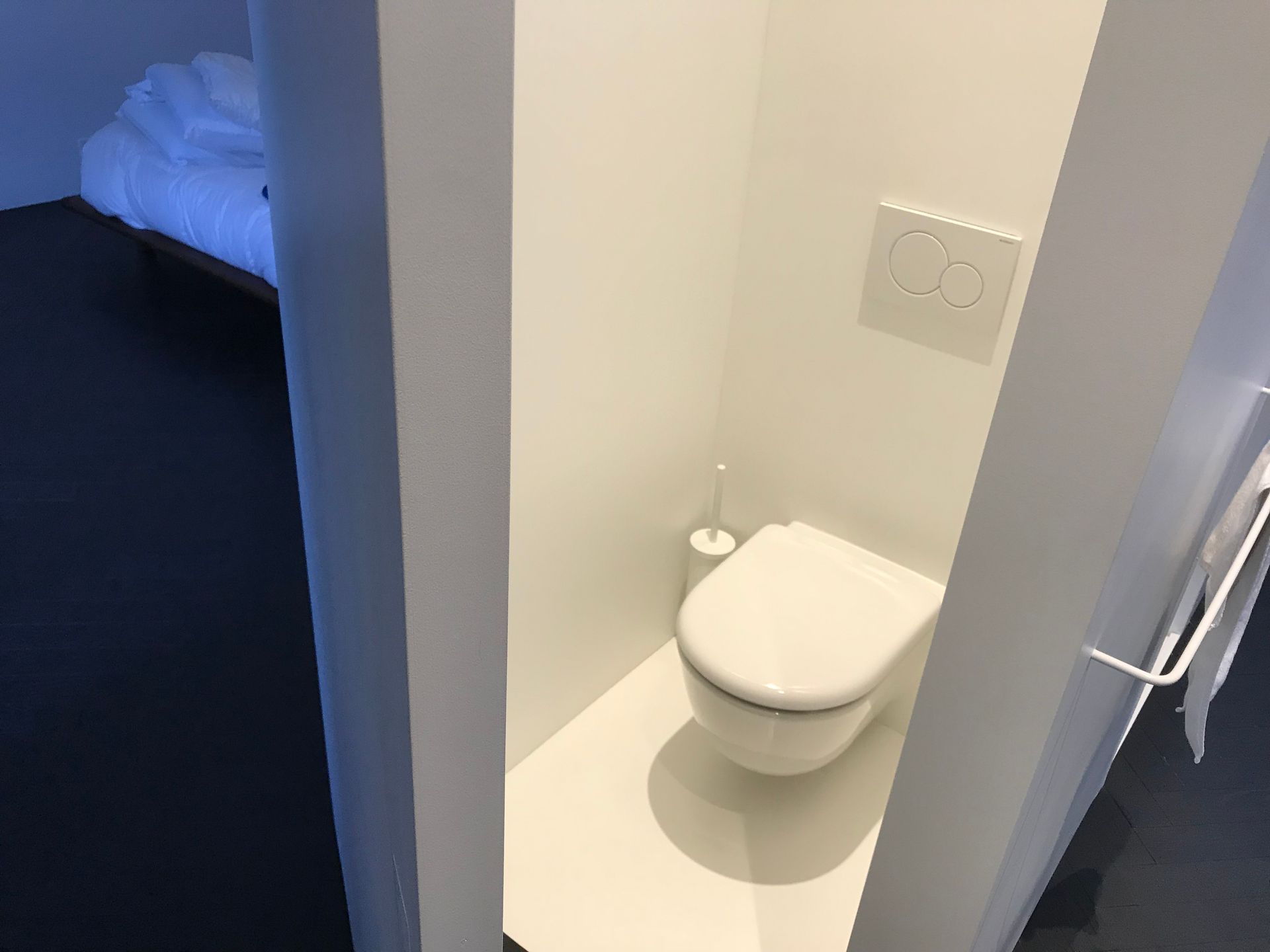 Petite salle de bains avec toilettes blanches murales dans une étroite alcôve à côté d'une porte de chambre.