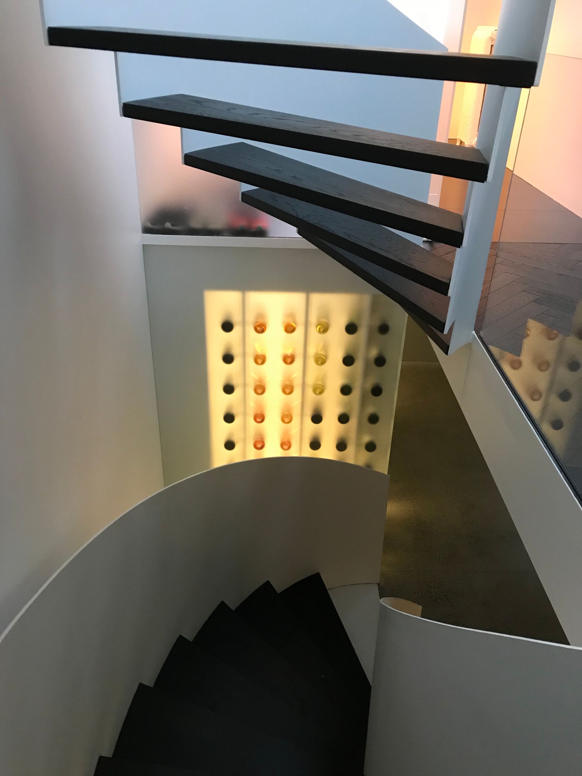 Escalier en colimaçon avec des marches noires et un mur illuminé de lumières colorées en dessous.