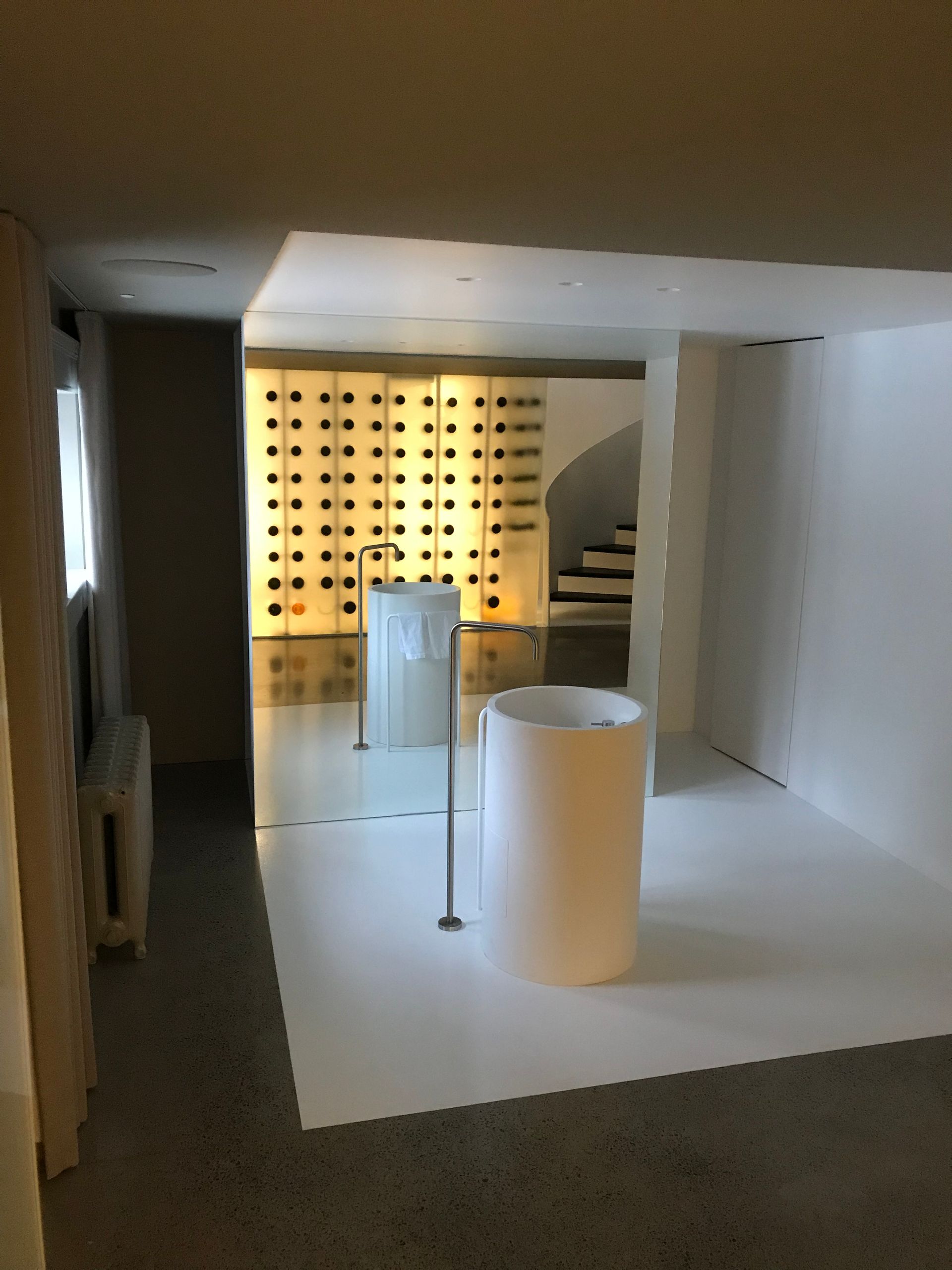 Intérieur minimaliste moderne avec des socles blancs, un éclairage mural et un escalier courbe.