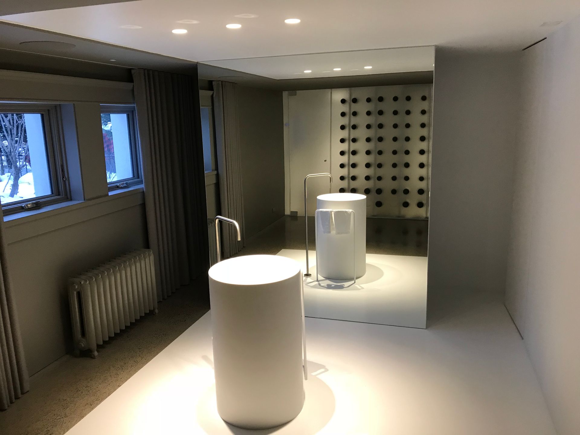 Salle de bains moderne avec deux lavabos blancs sur pied, fenêtres, radiateur et éclairage encastré