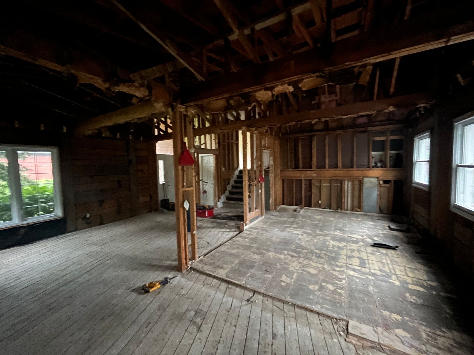 Pièce vide et inachevée avec charpente apparente, parquet usé et fenêtres laissant entrer la lumière du jour