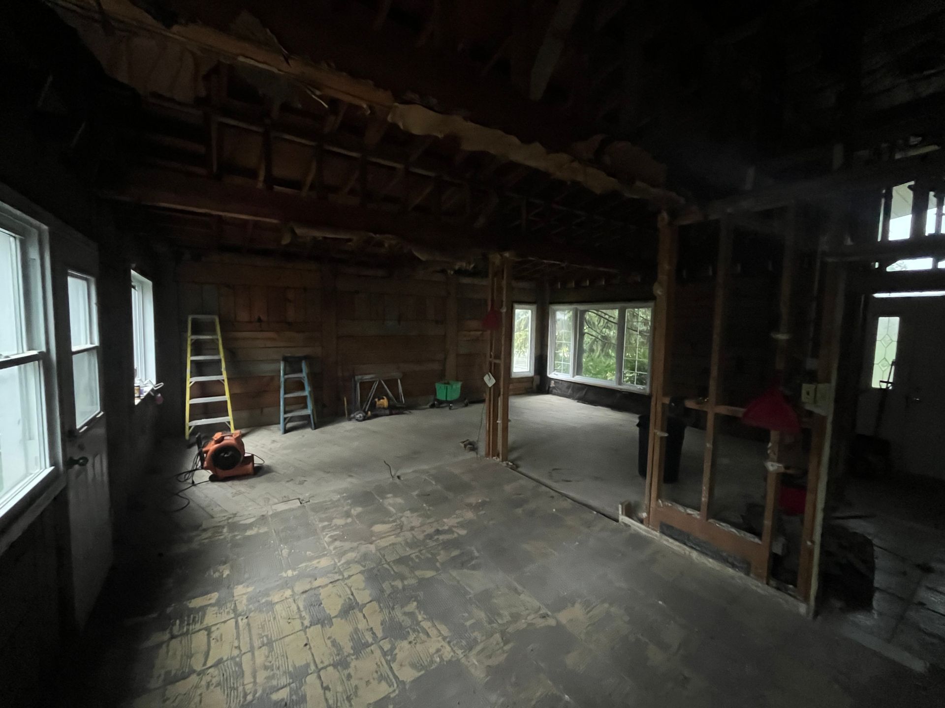 Pièce vide et inachevée avec poutres apparentes, une échelle et des outils de construction sur un sol usé