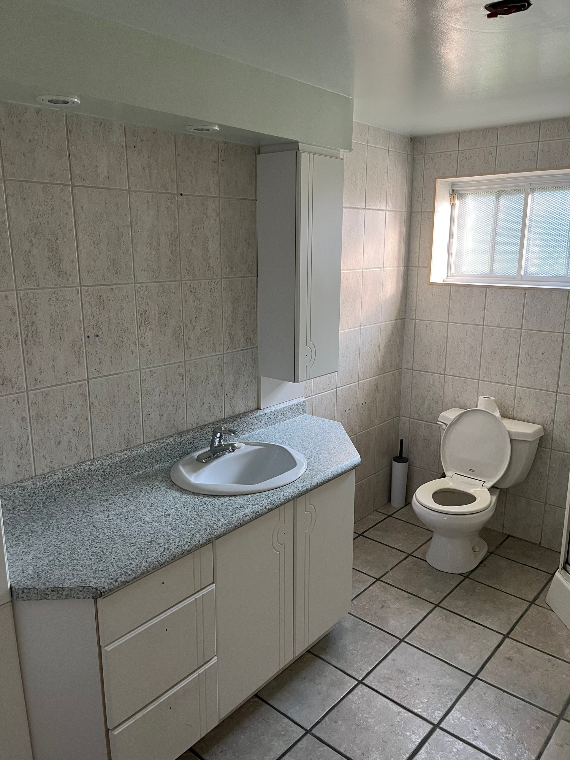 Petite salle de bains avec lavabo, sol carrelé, toilettes et fenêtre.