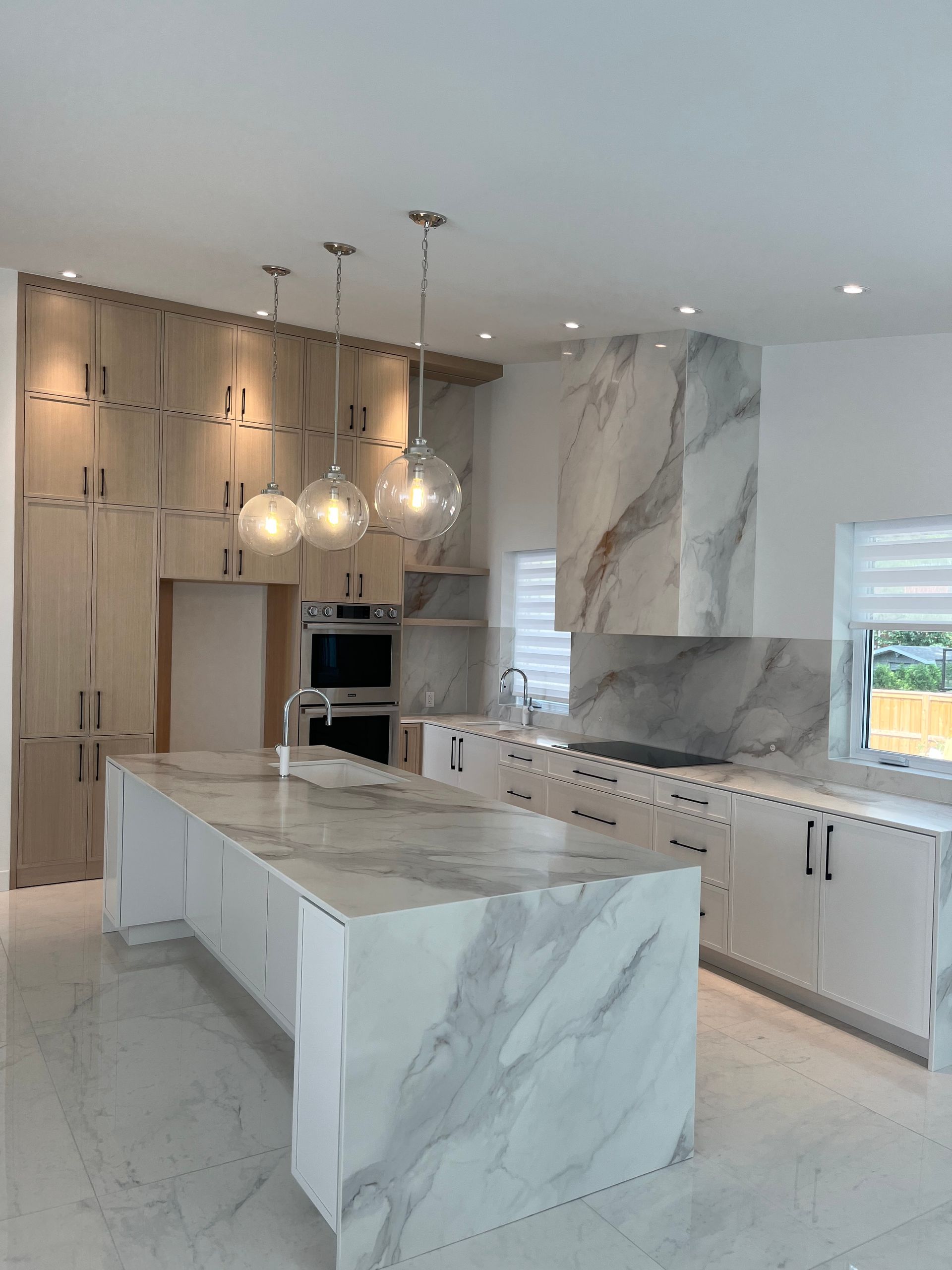Cuisine moderne en marbre avec îlot central en cascade, luminaires suspendus et armoires blanches.