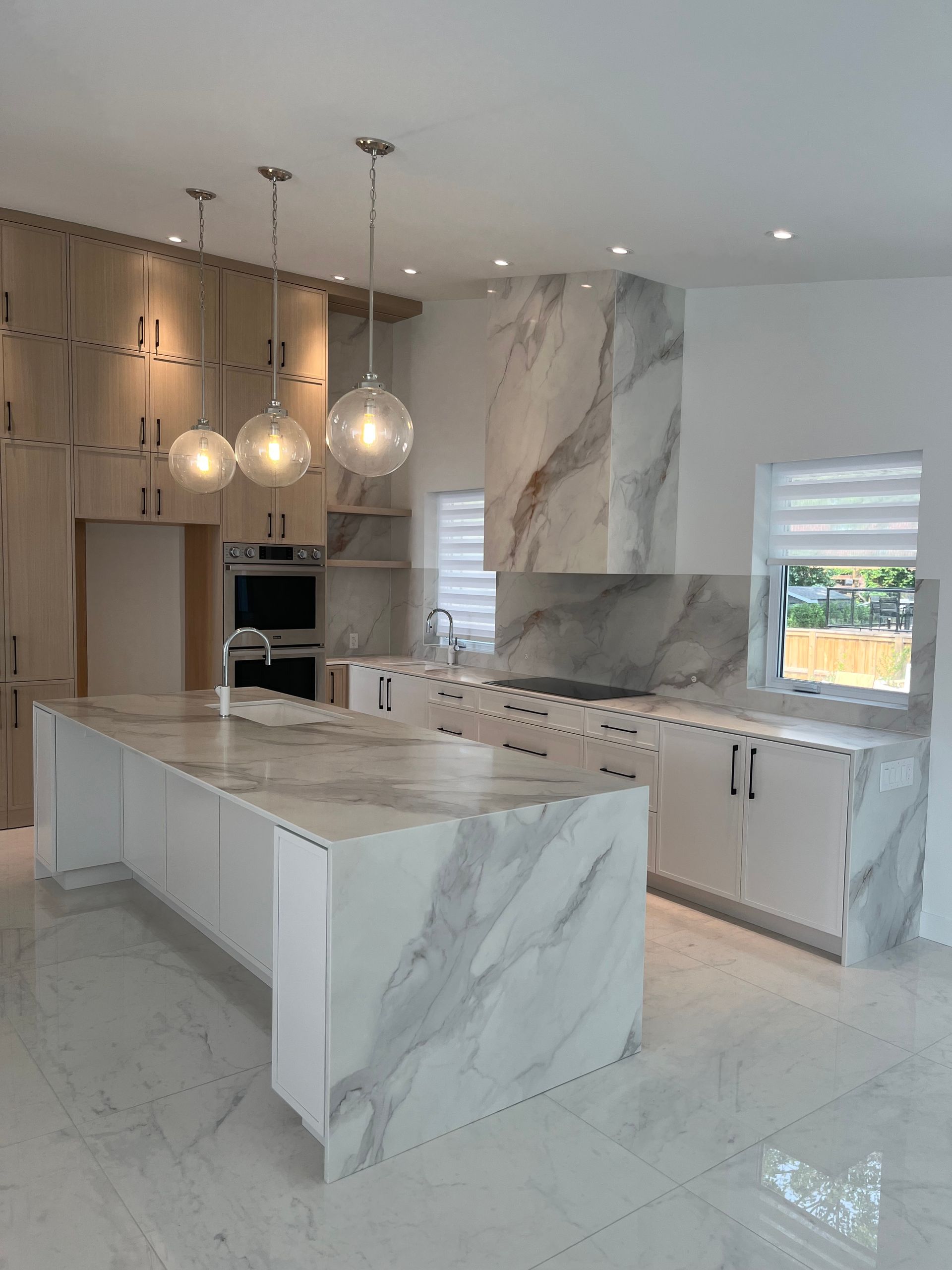 Cuisine moderne en marbre blanc avec grand îlot central, luminaires suspendus et appareils électroménagers intégrés