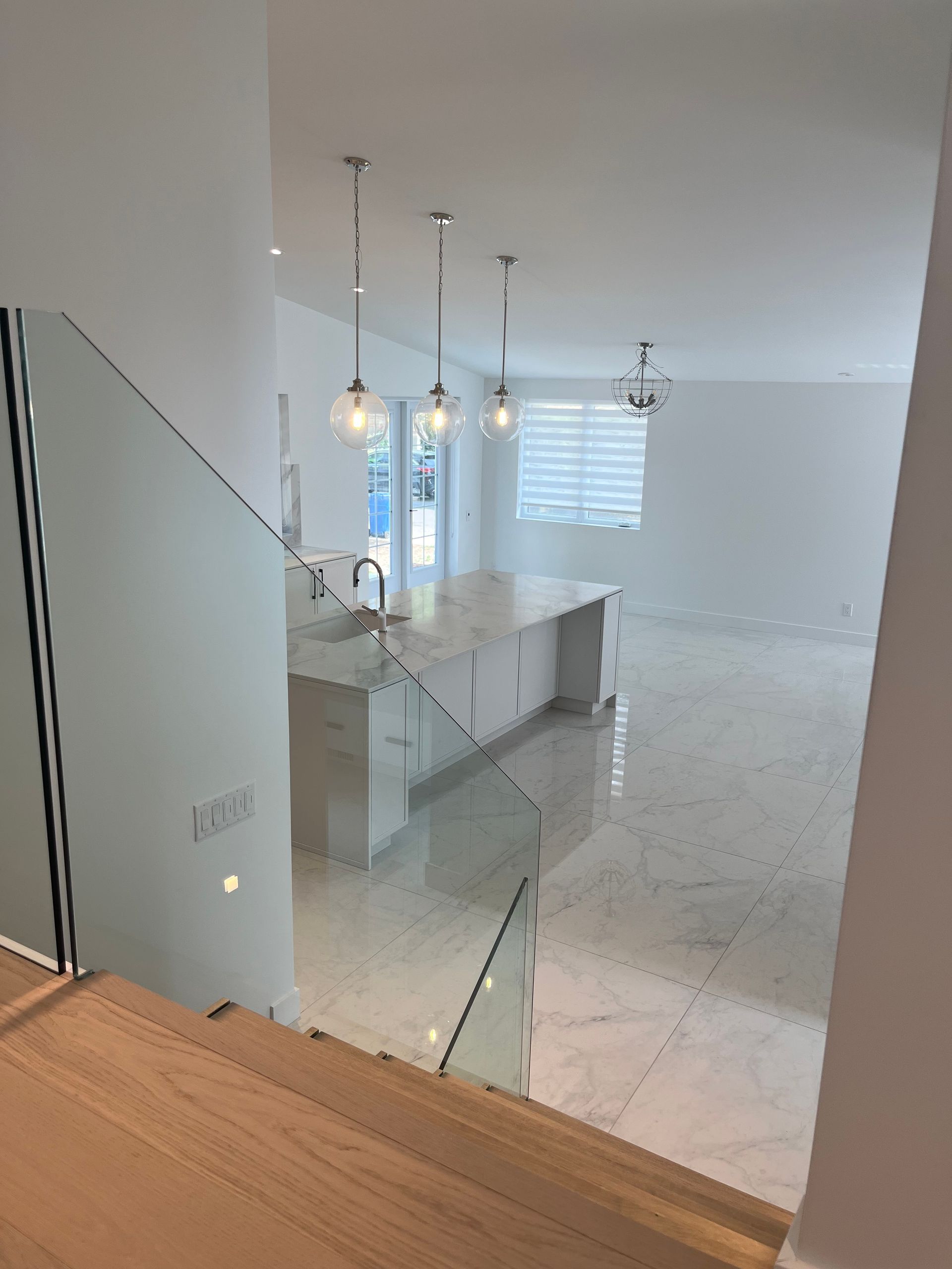 Cuisine et salle à manger modernes à aire ouverte avec sol carrelé blanc, escalier en verre et luminaires suspendus.