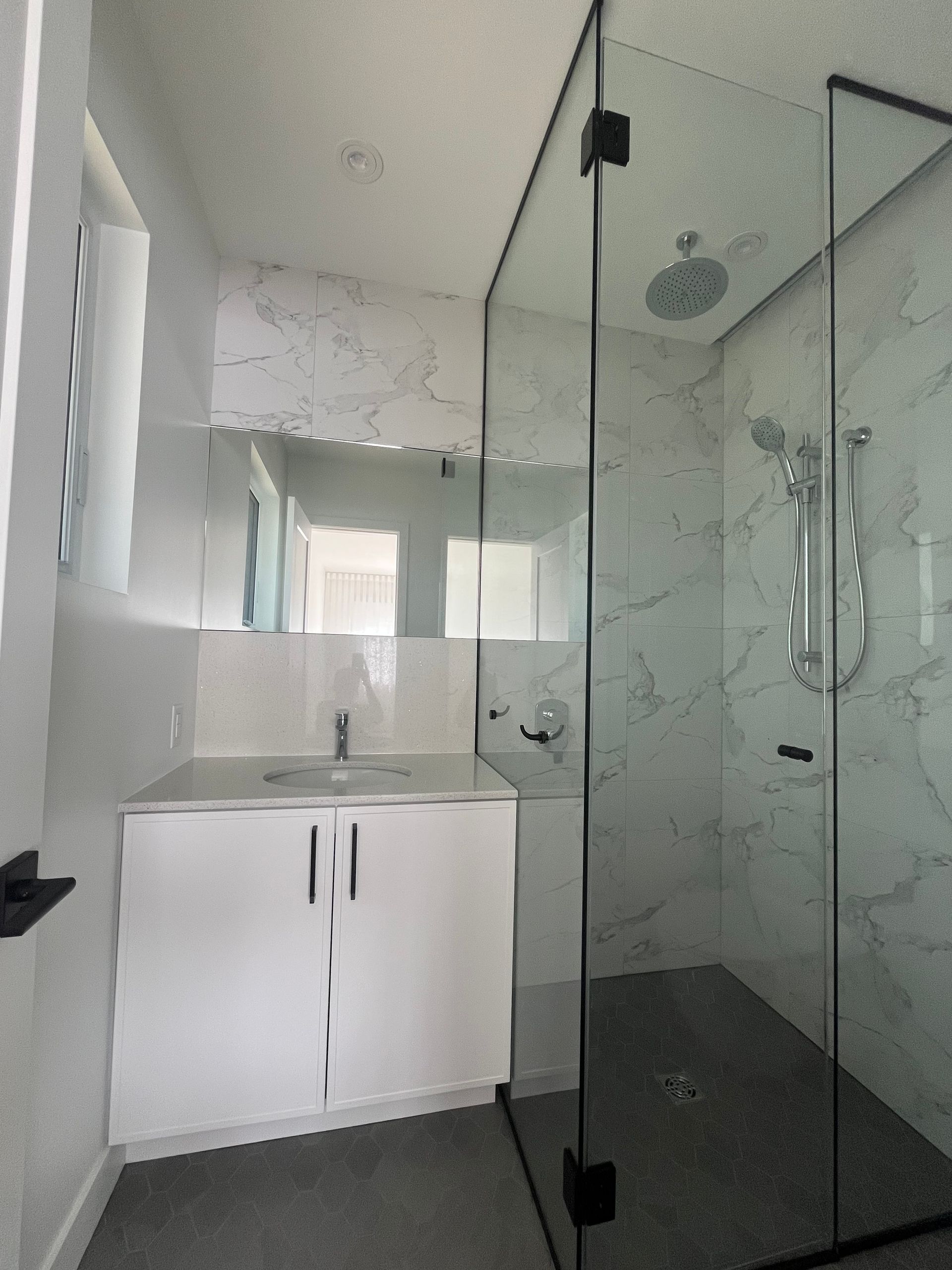 Salle de bains moderne avec double vasque, grand miroir et douche vitrée dans des tons blancs et noirs.