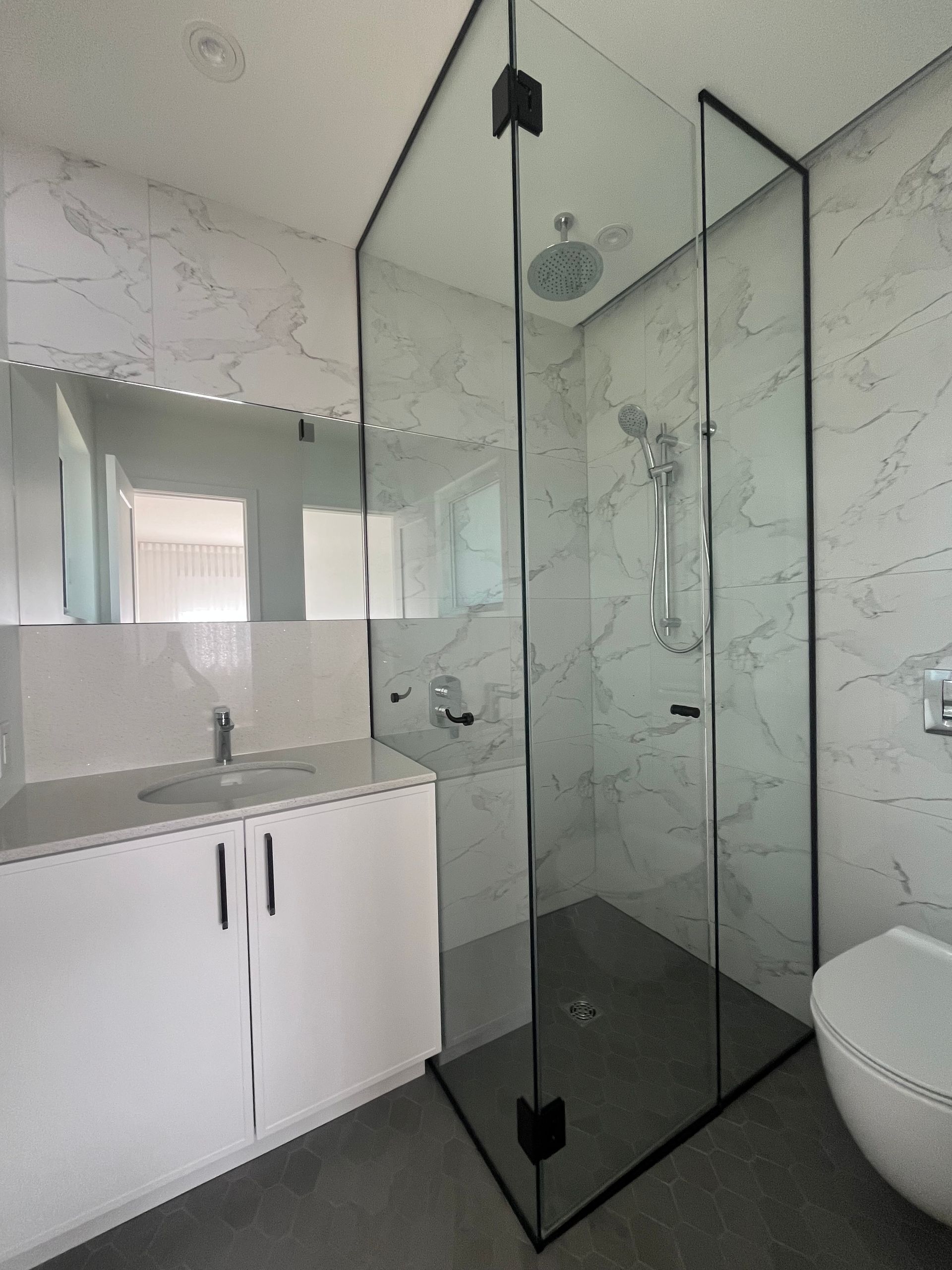 Salle de bains moderne avec meuble-lavabo blanc, grand miroir, douche à l'italienne avec cadre en verre noir et toilettes