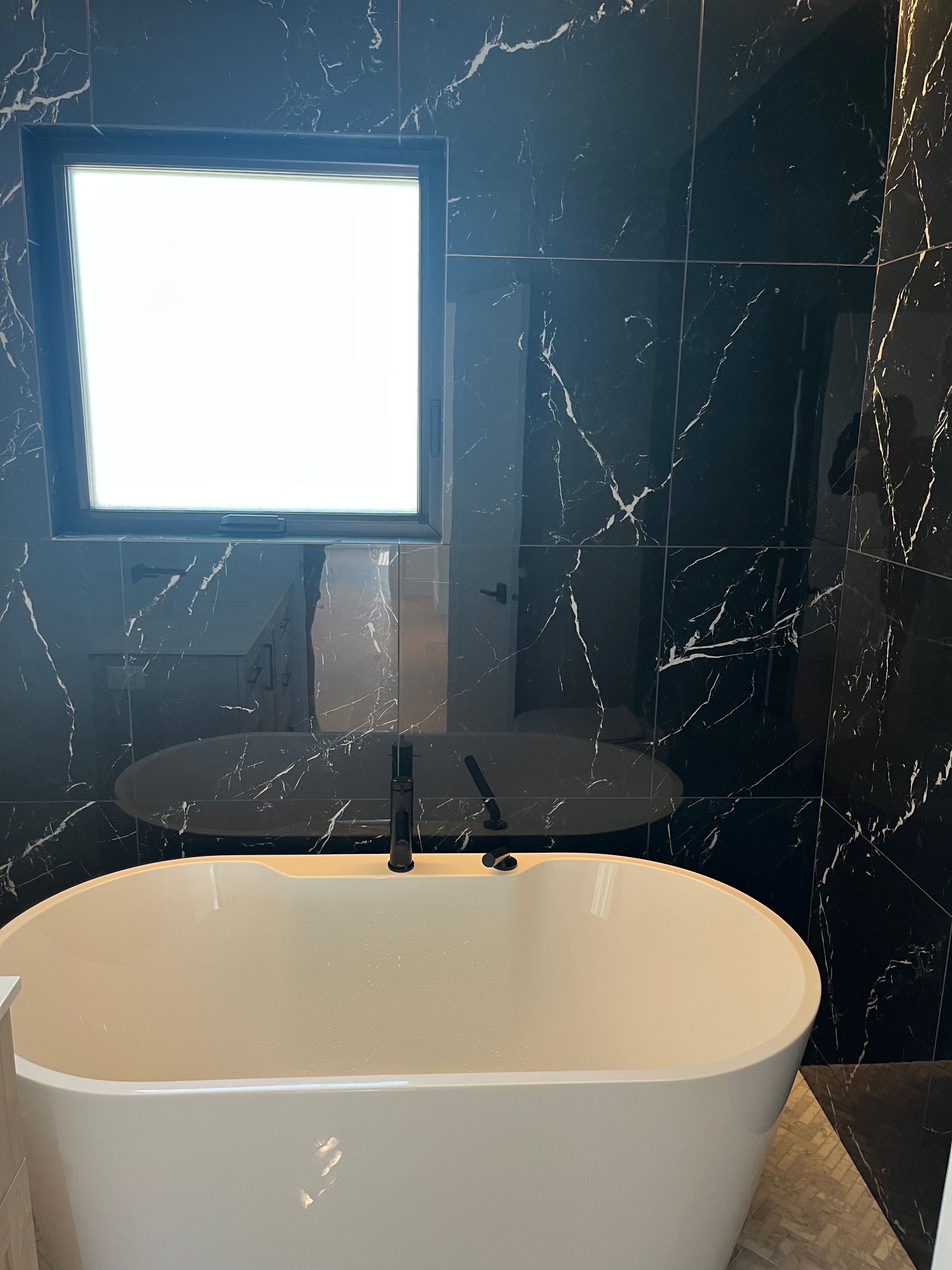 Meuble-lavabo moderne avec miroir éclairé, mur en marbre noir et lavabo ovale blanc