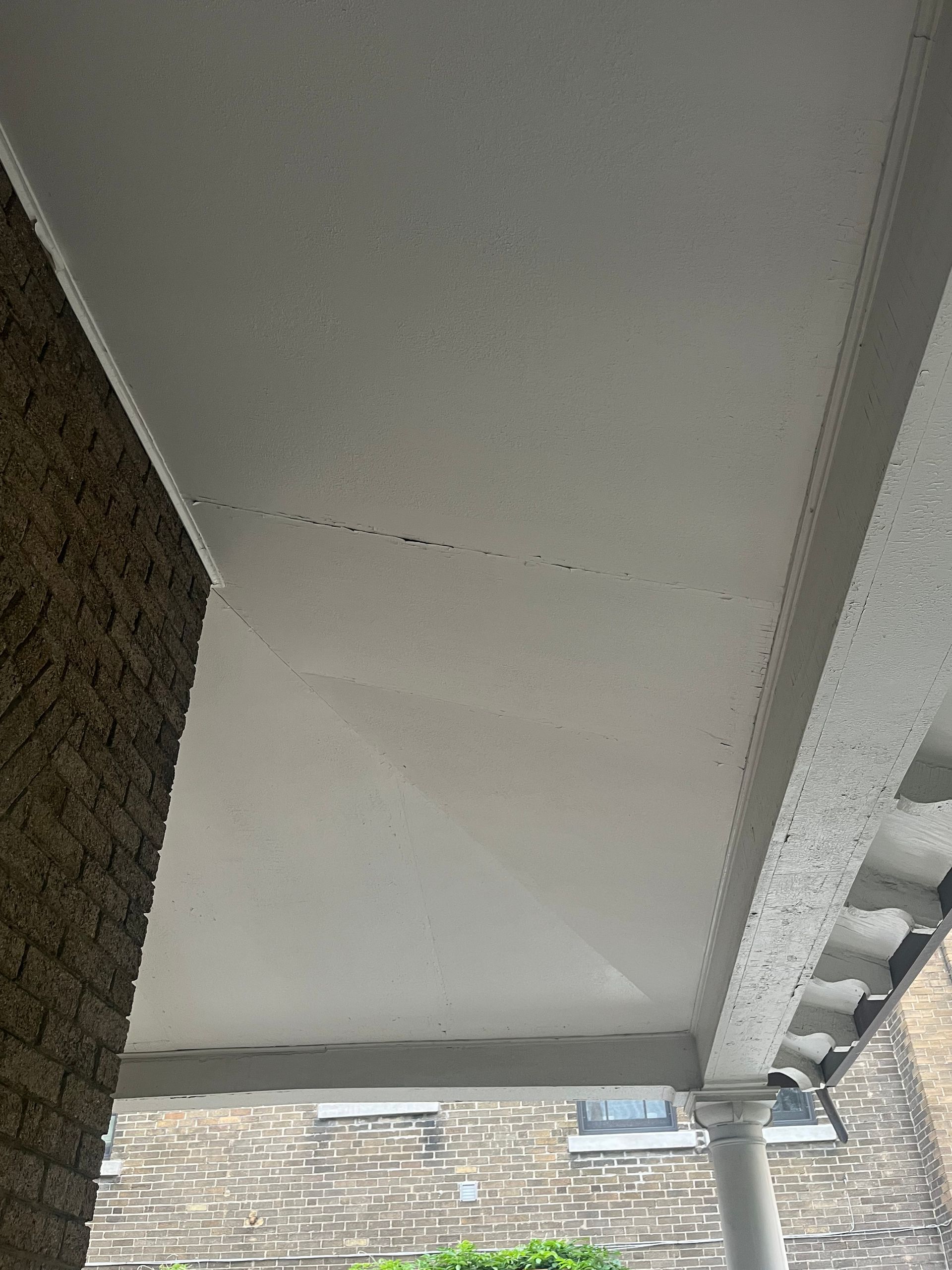 Dessous d'un auvent ou d'un plafond blanc avec une jointure fissurée et un mur en pierre à gauche.