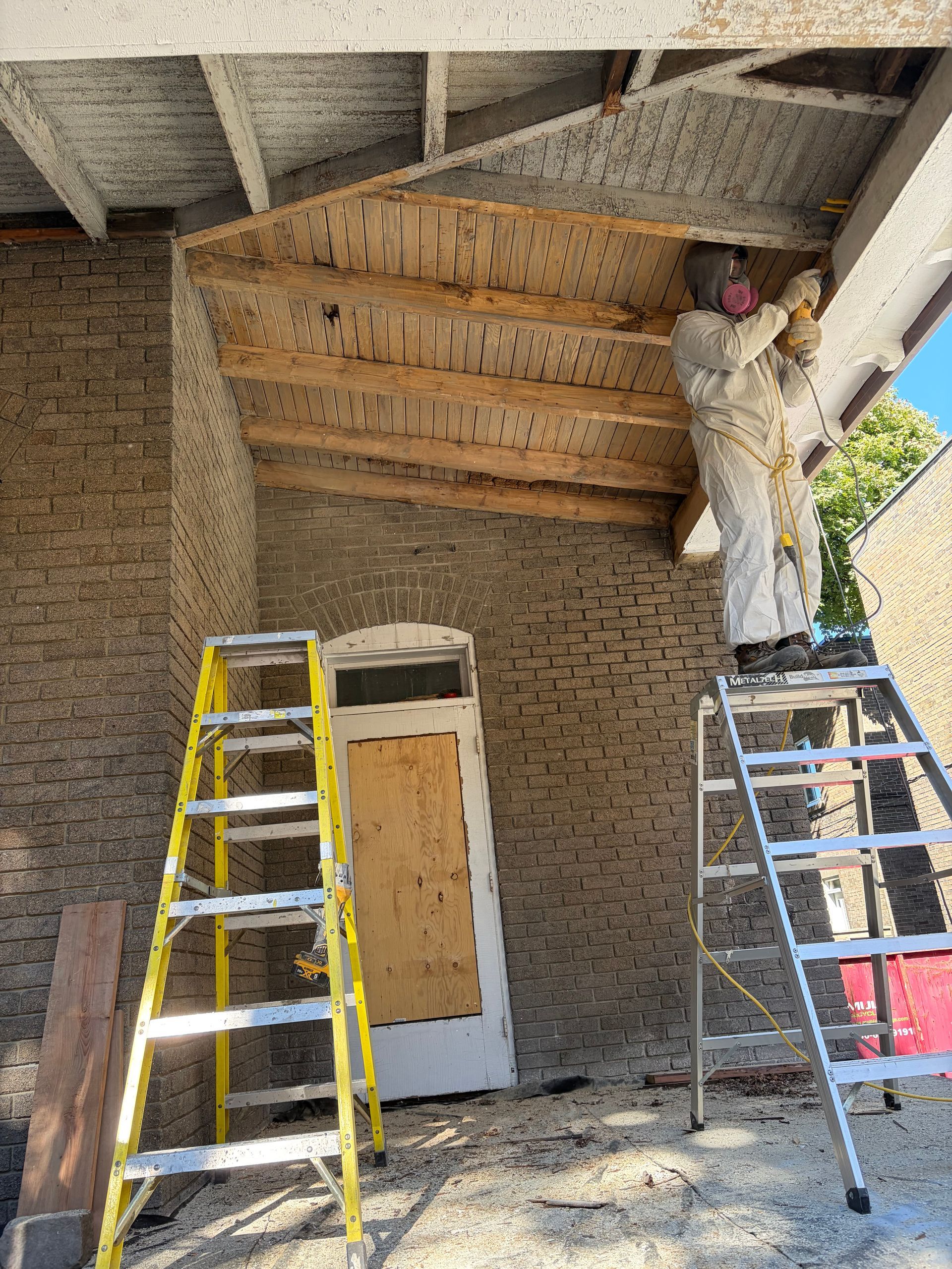 Un ouvrier peint un plafond au-dessus de deux échelles à l'entrée d'un bâtiment