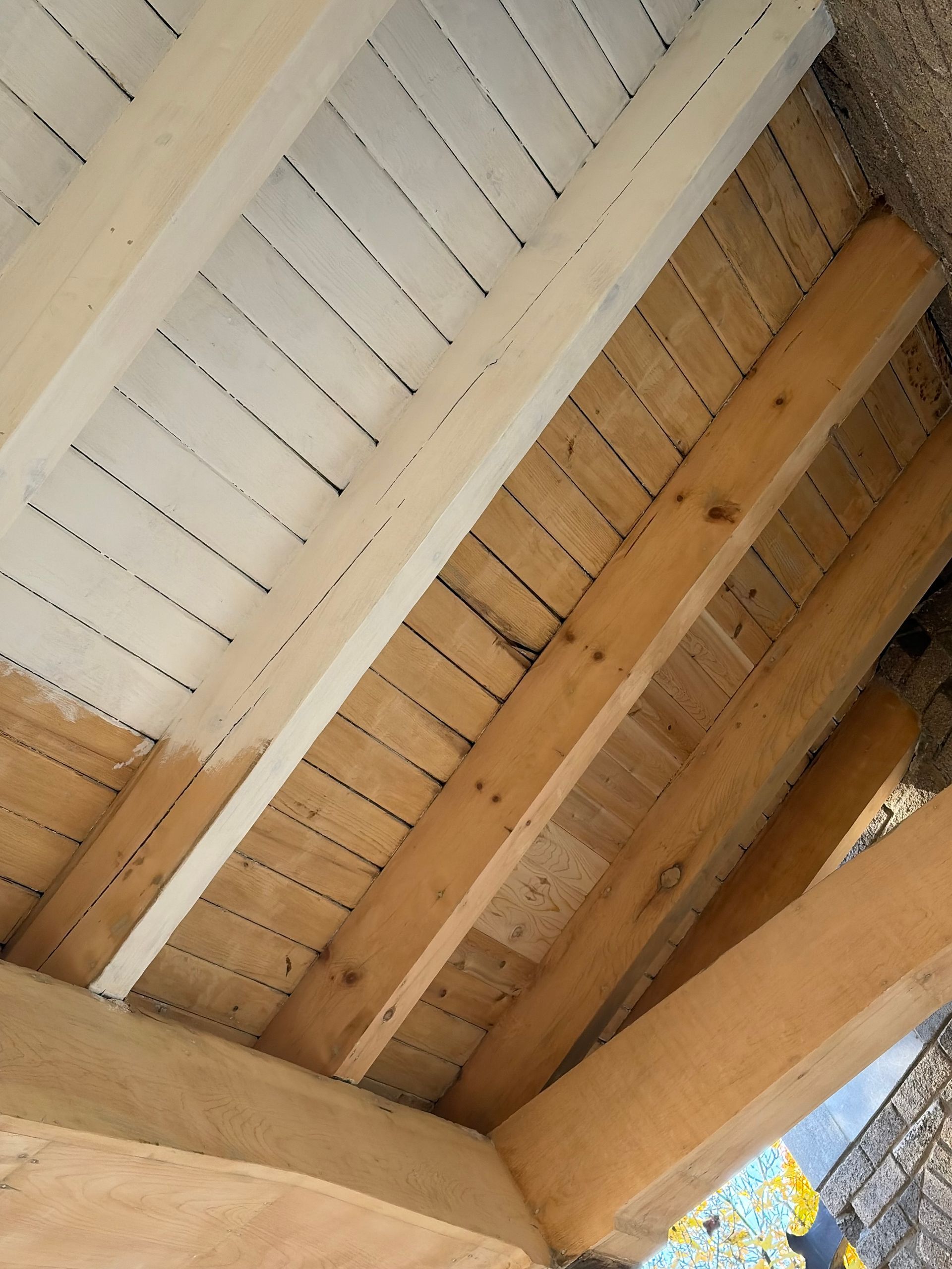 Gros plan sur le plafond d'une véranda en bois avec des lattes et des poutres blanches, laissant apparaître le ciel bleu sur le bord.