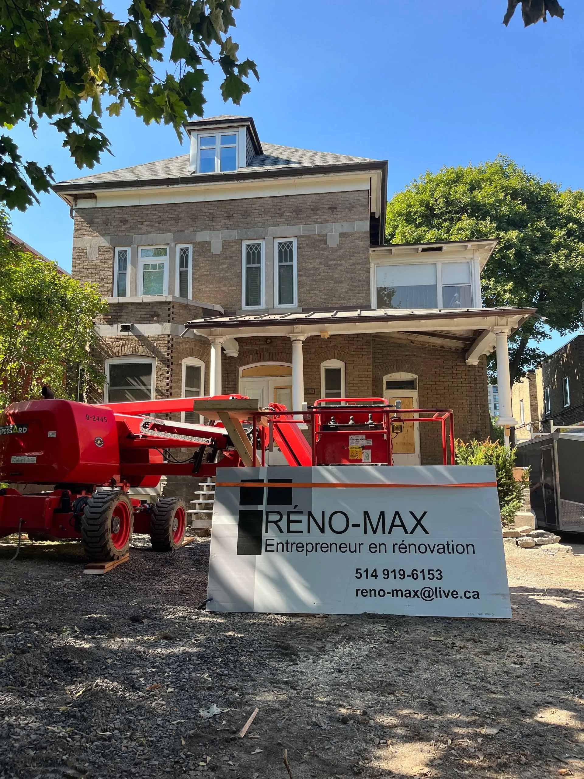 Maison en pierre en rénovation avec des équipements de levage rouges et une bannière RENO-MAX devant